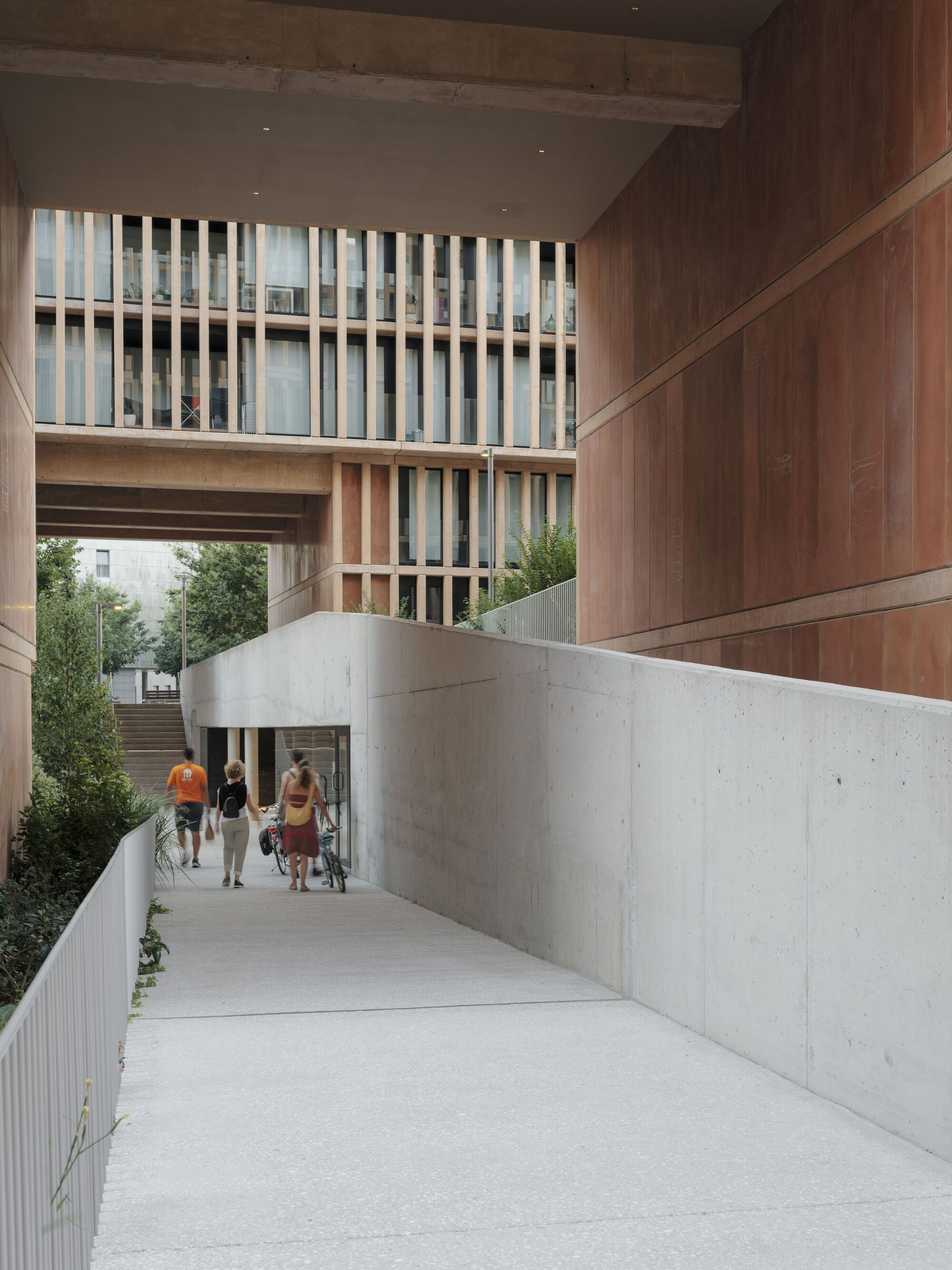 Sloped concrete passage with timber-clad soffit overhead and pedestrians approaching the walkway
