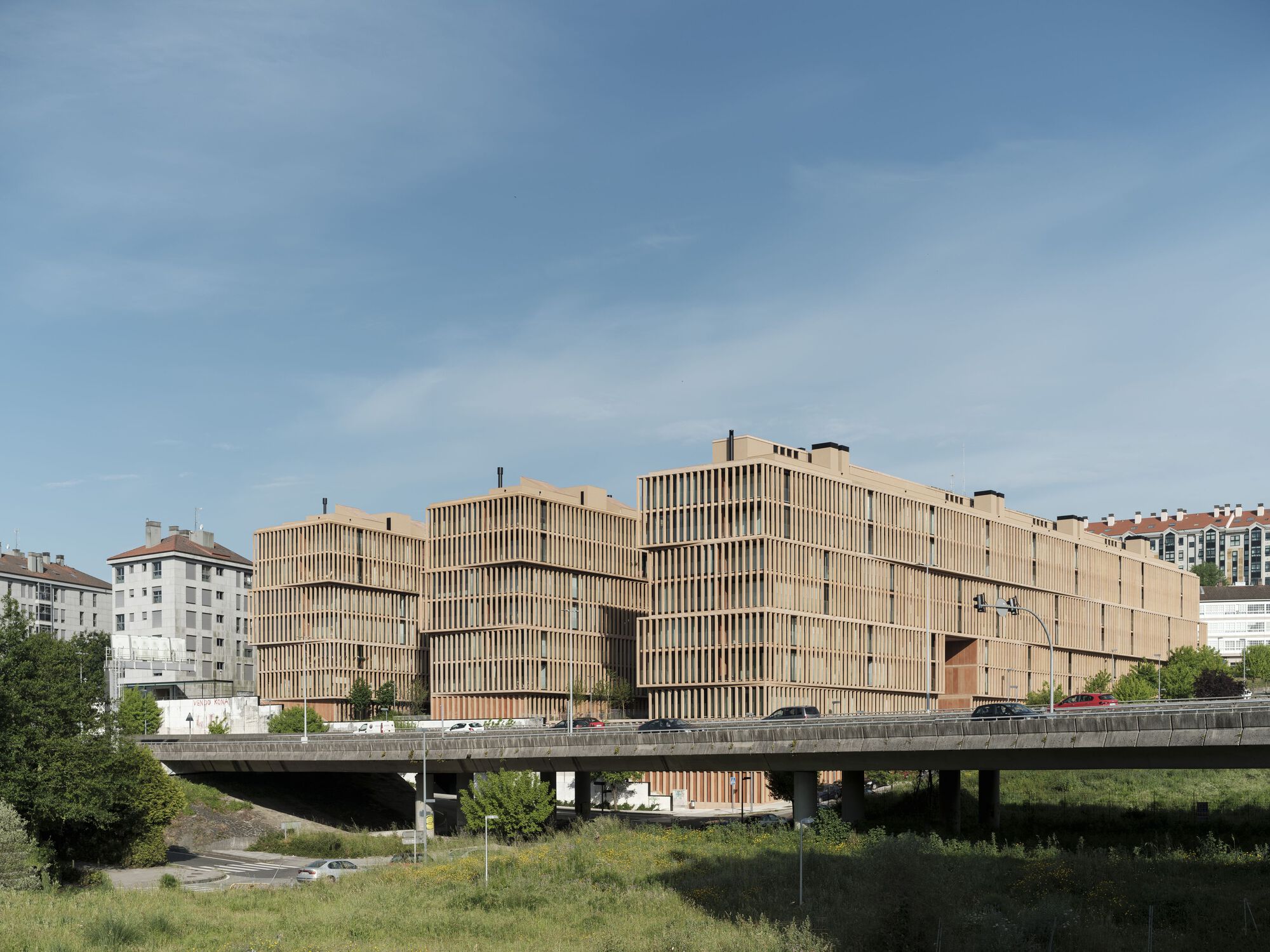 Long view of the timber-clad volume from across the concrete bridge and roadway