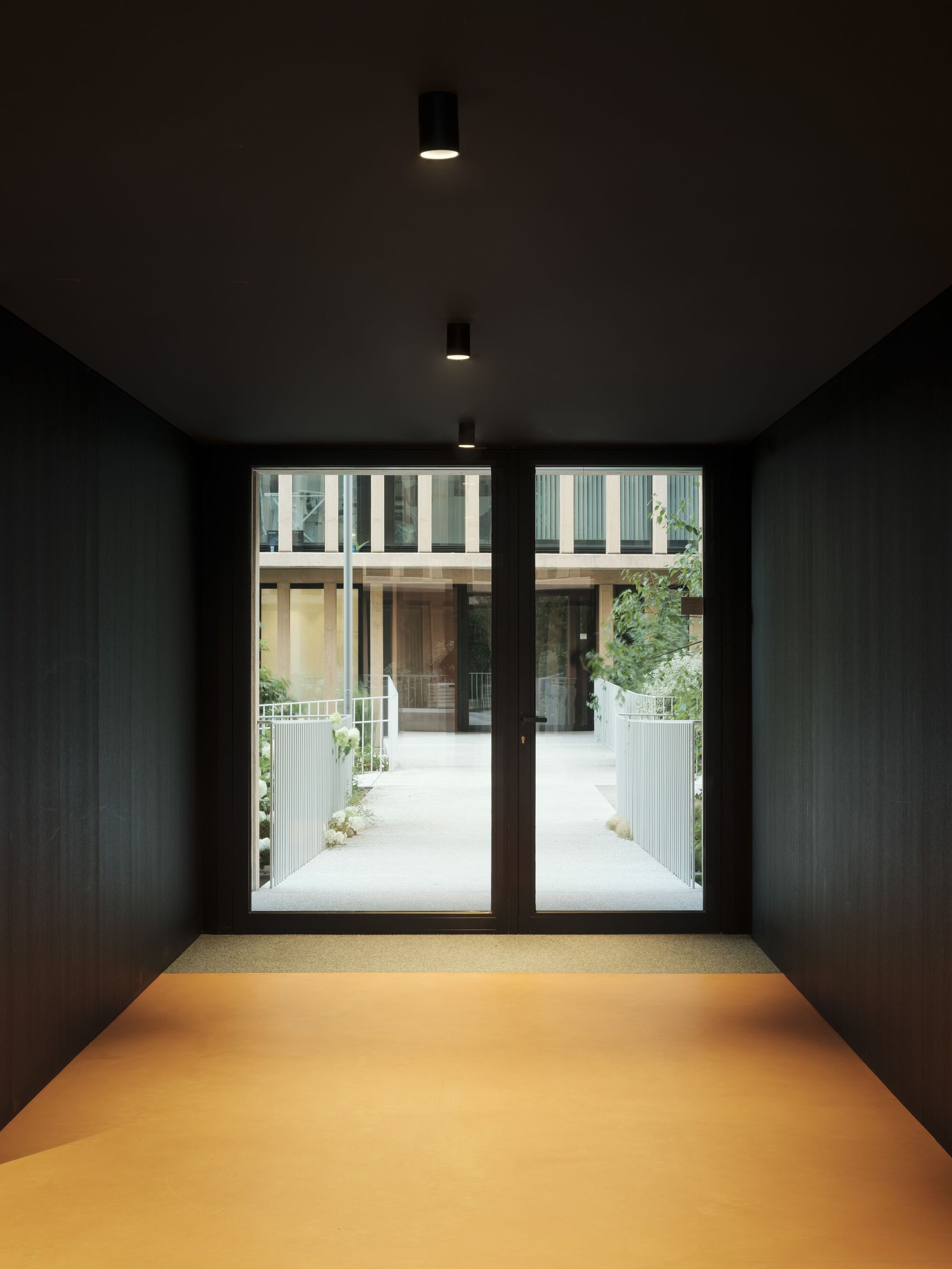 Dark vestibule with yellow resin floor and glass doors leading to the sunlit courtyard