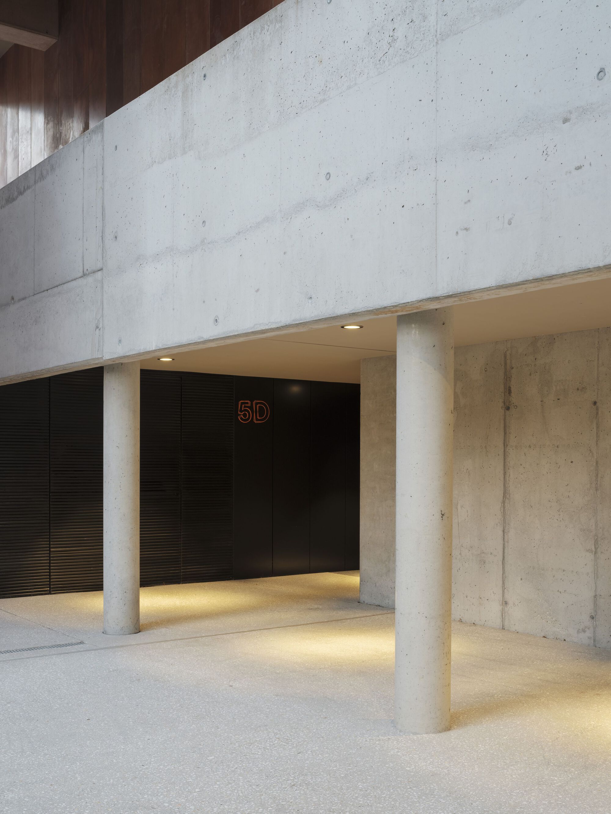 Concrete lobby with cylindrical columns and strip lighting beneath the ceiling soffit