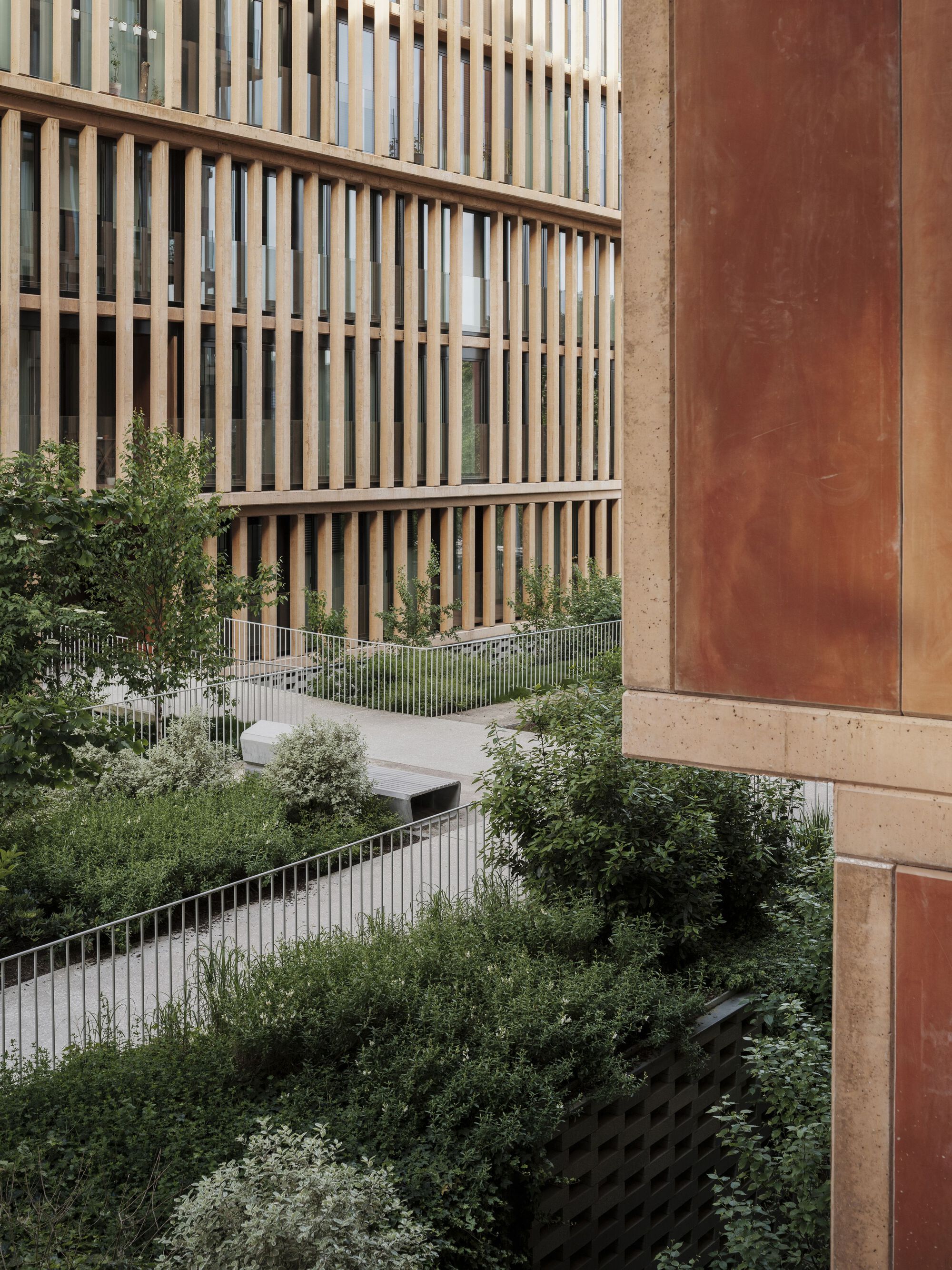 Terraced planted balconies with metal railings between timber screened facades and weathered steel panels