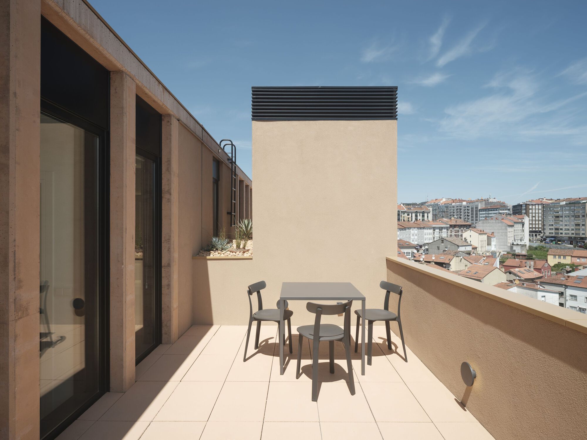Rooftop terrace with dining furniture overlooking residential buildings under a clear blue sky