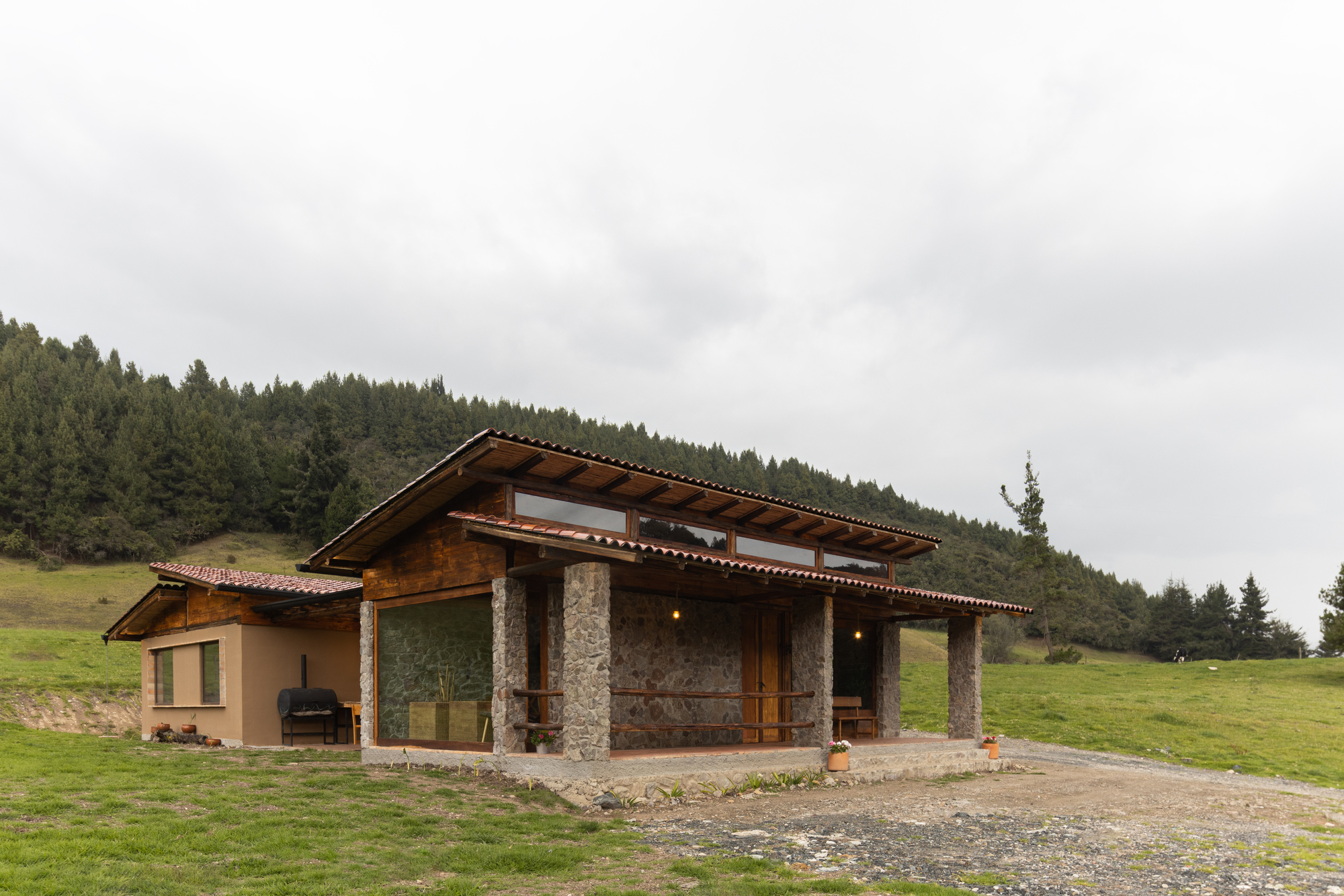 Exterior view of the stone and timber structure with wide eaves against forested hillside under grey skies