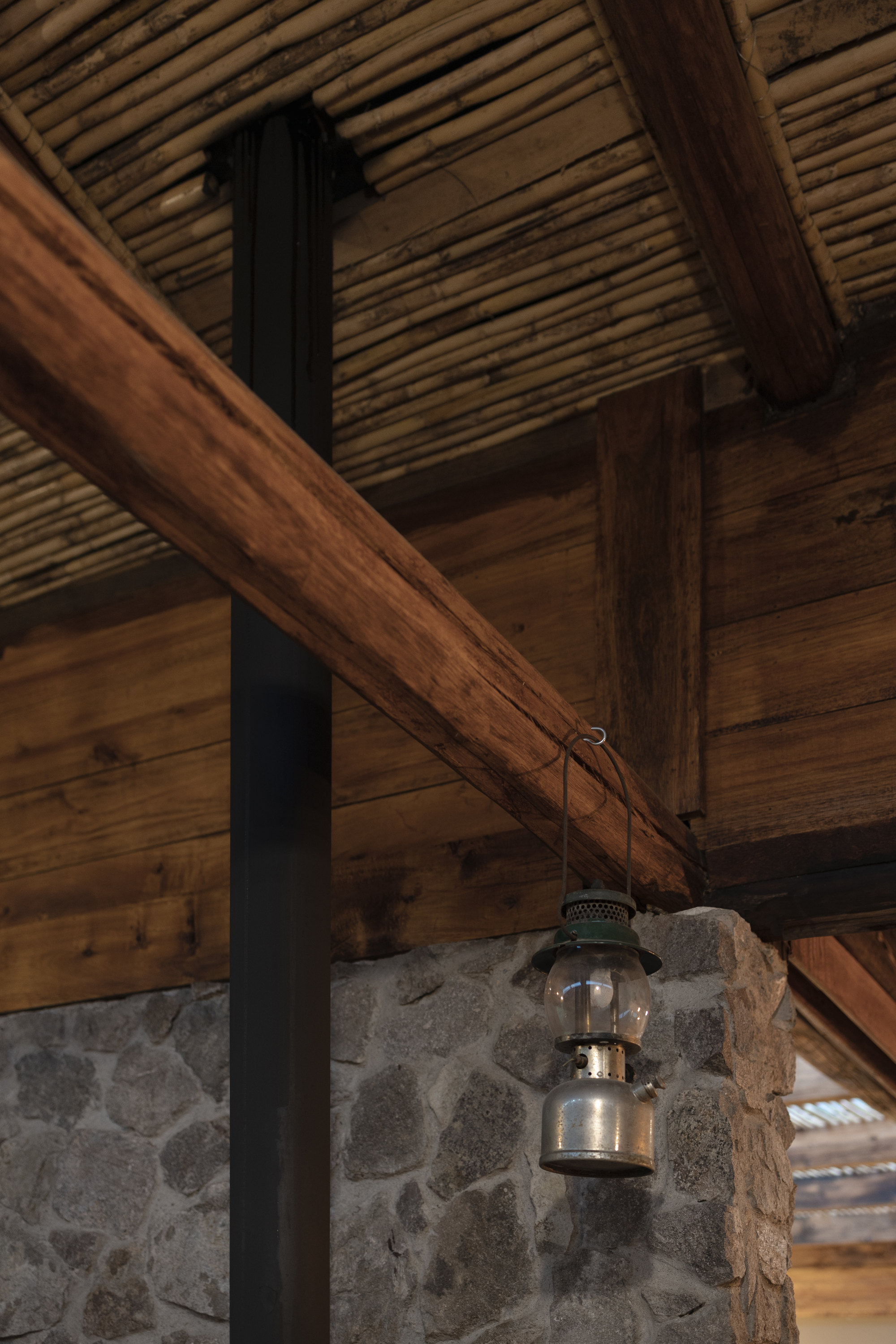 Detail of a vintage lantern hanging from timber beams above a stone and metal column junction