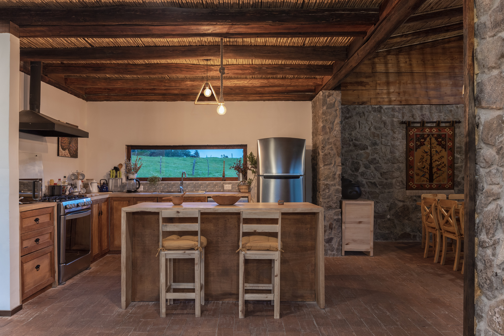 Open kitchen with timber island, stone walls, and exposed beam ceiling with pendant light