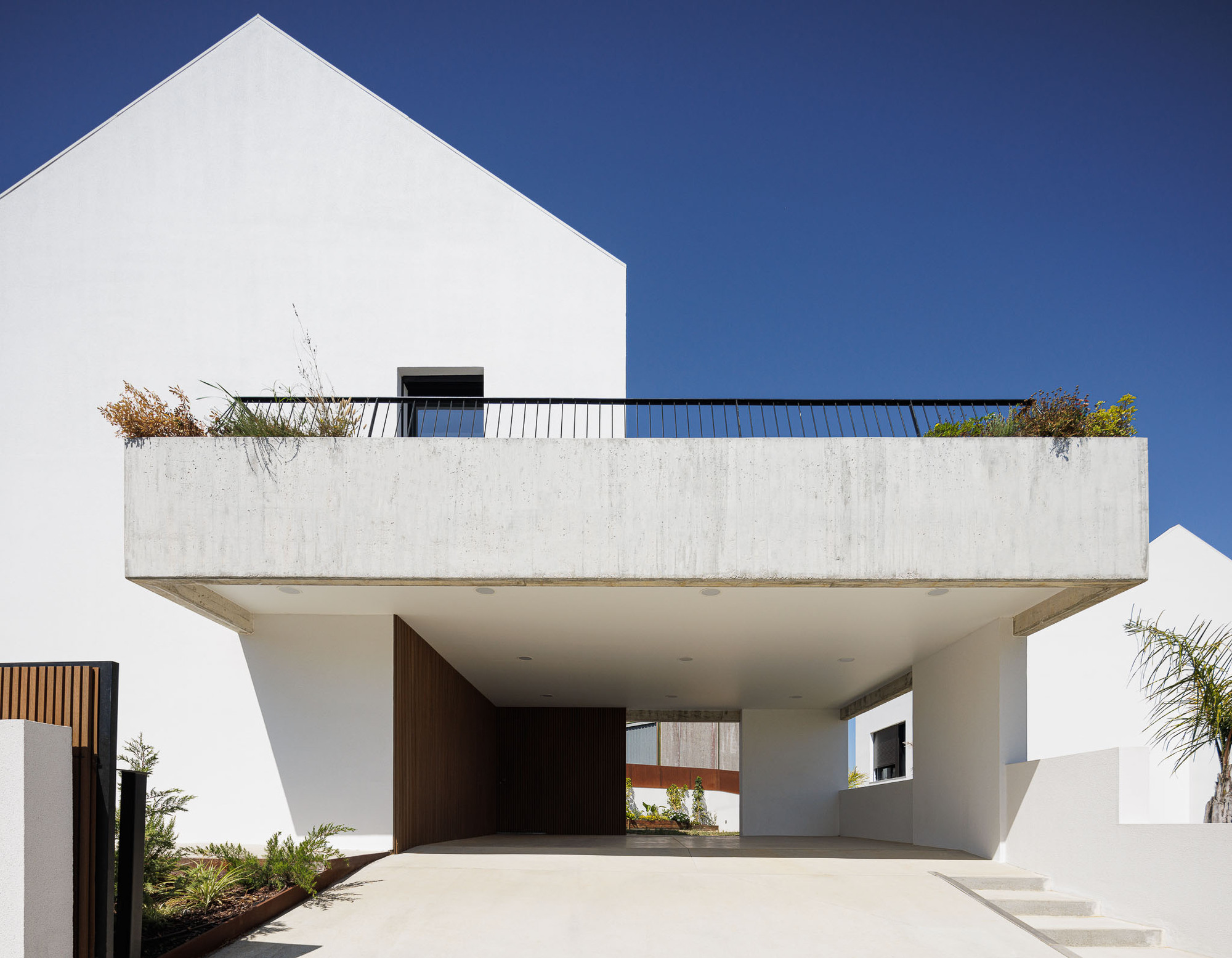 Cantilevered concrete terrace with integrated planter above a recessed entry carport in bright midday sun