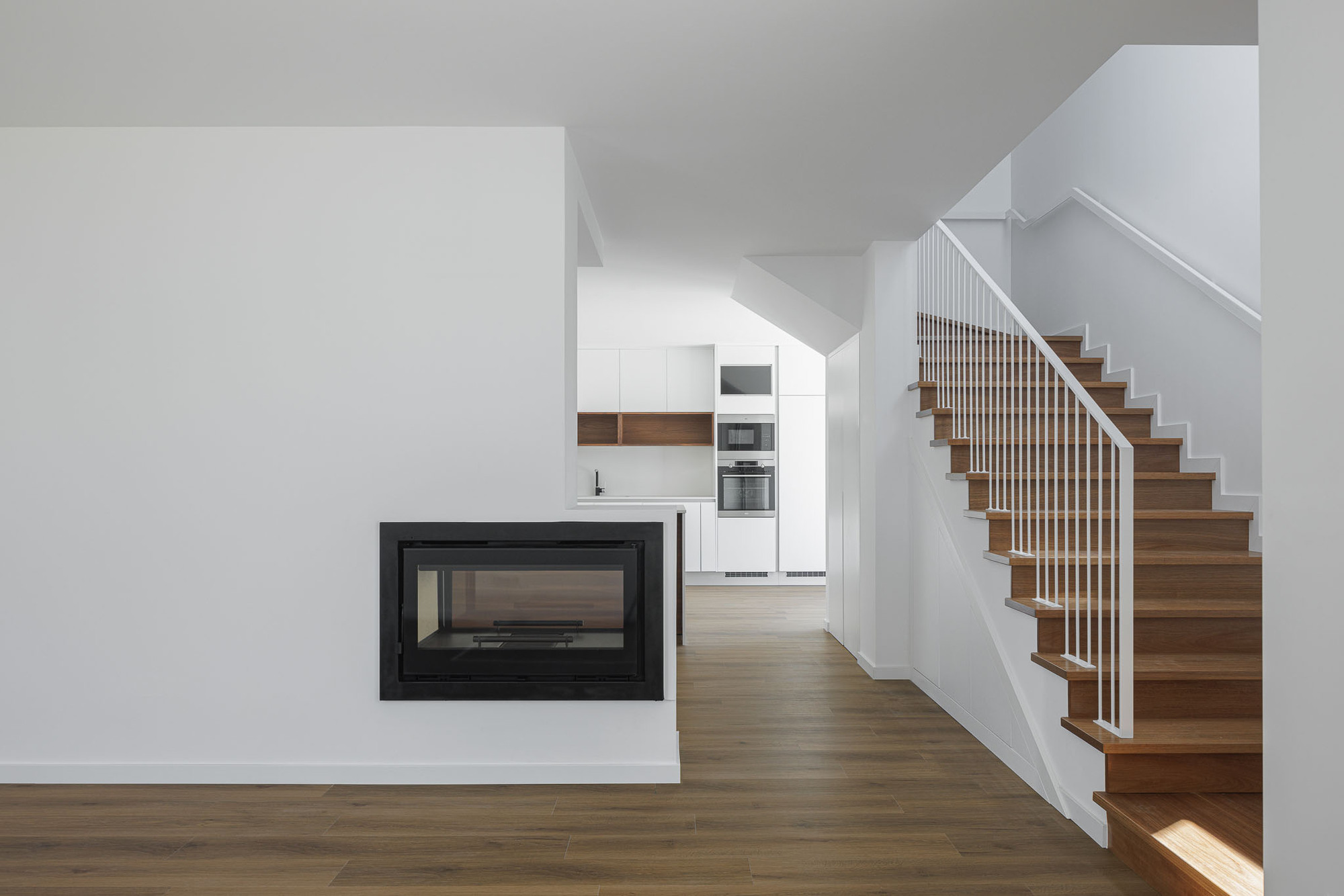Open living space with timber staircase, vertical white balusters, and recessed black fireplace insert