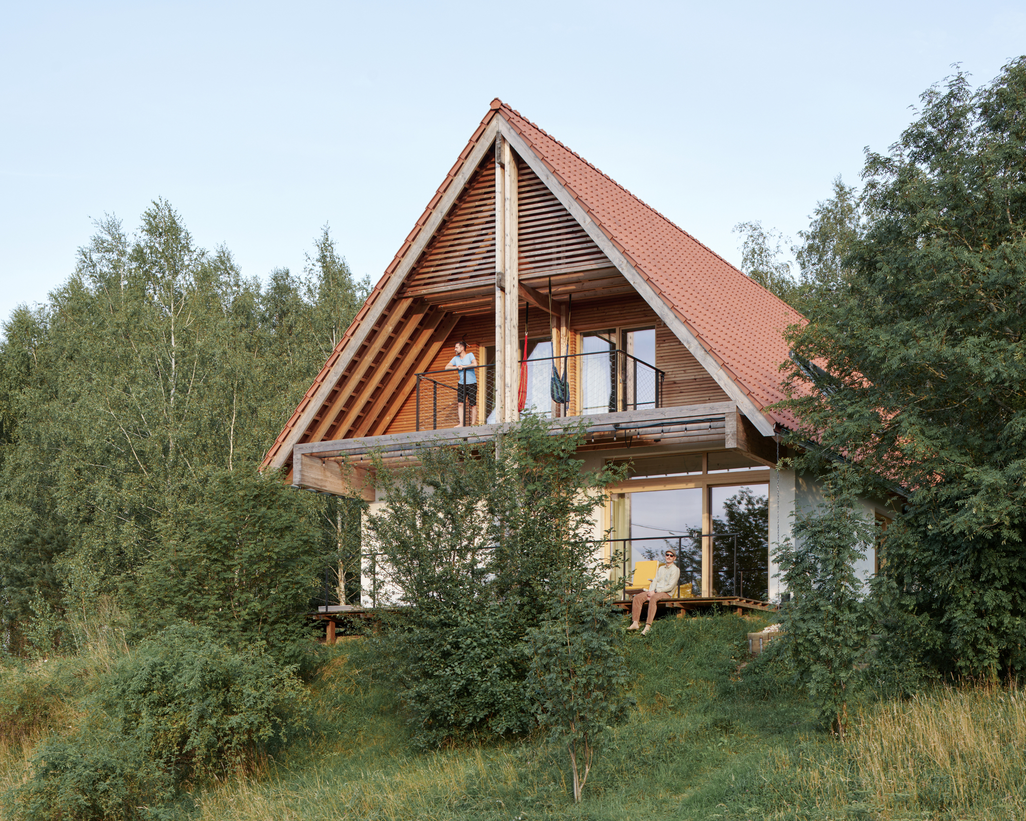 Two-story timber structure with steep red tile roof and exposed balcony framed by birch trees