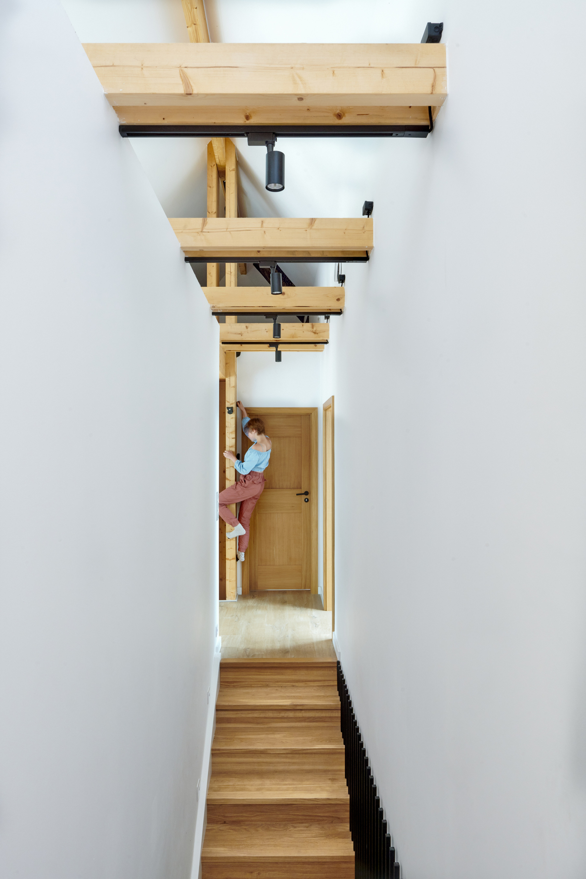 Vertical view up the timber stairwell with exposed beams and a figure pausing at the landing