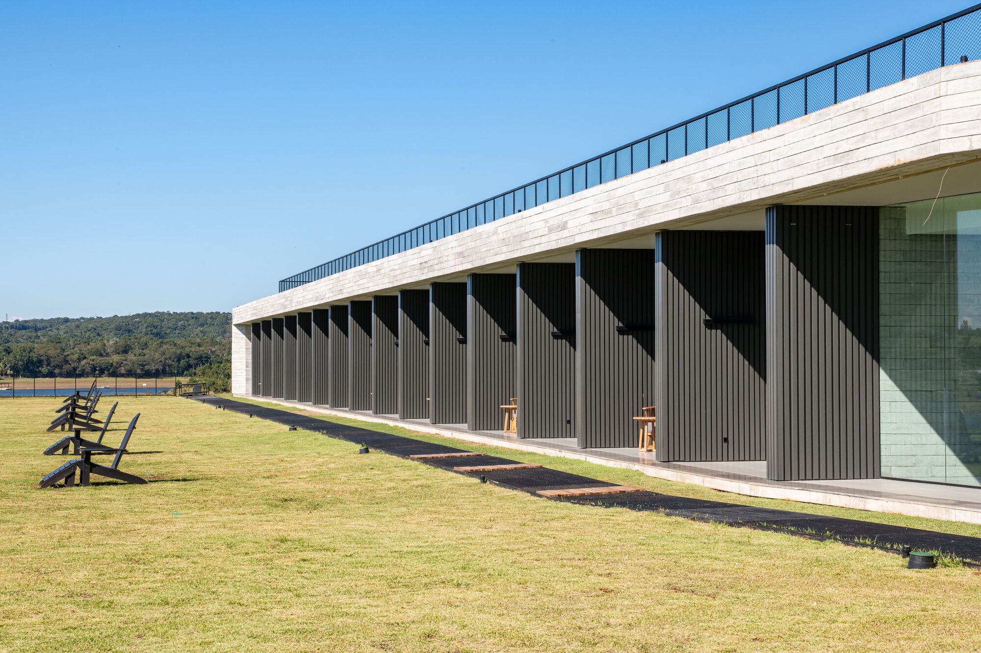 Facade with vertical timber battens below a white brick parapet and sloped green roof under clear sky