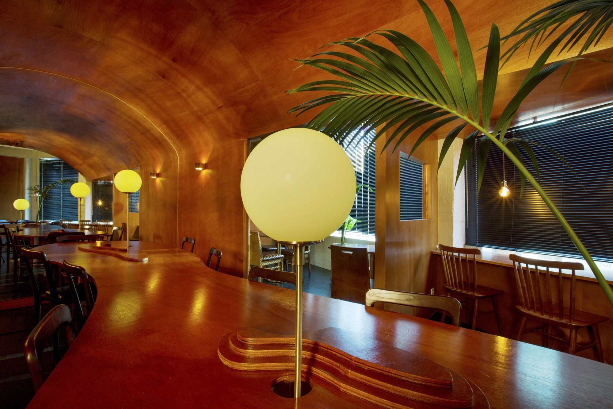 Interior dining space with laminated wood vault ceiling and spherical pendant lamps at twilight