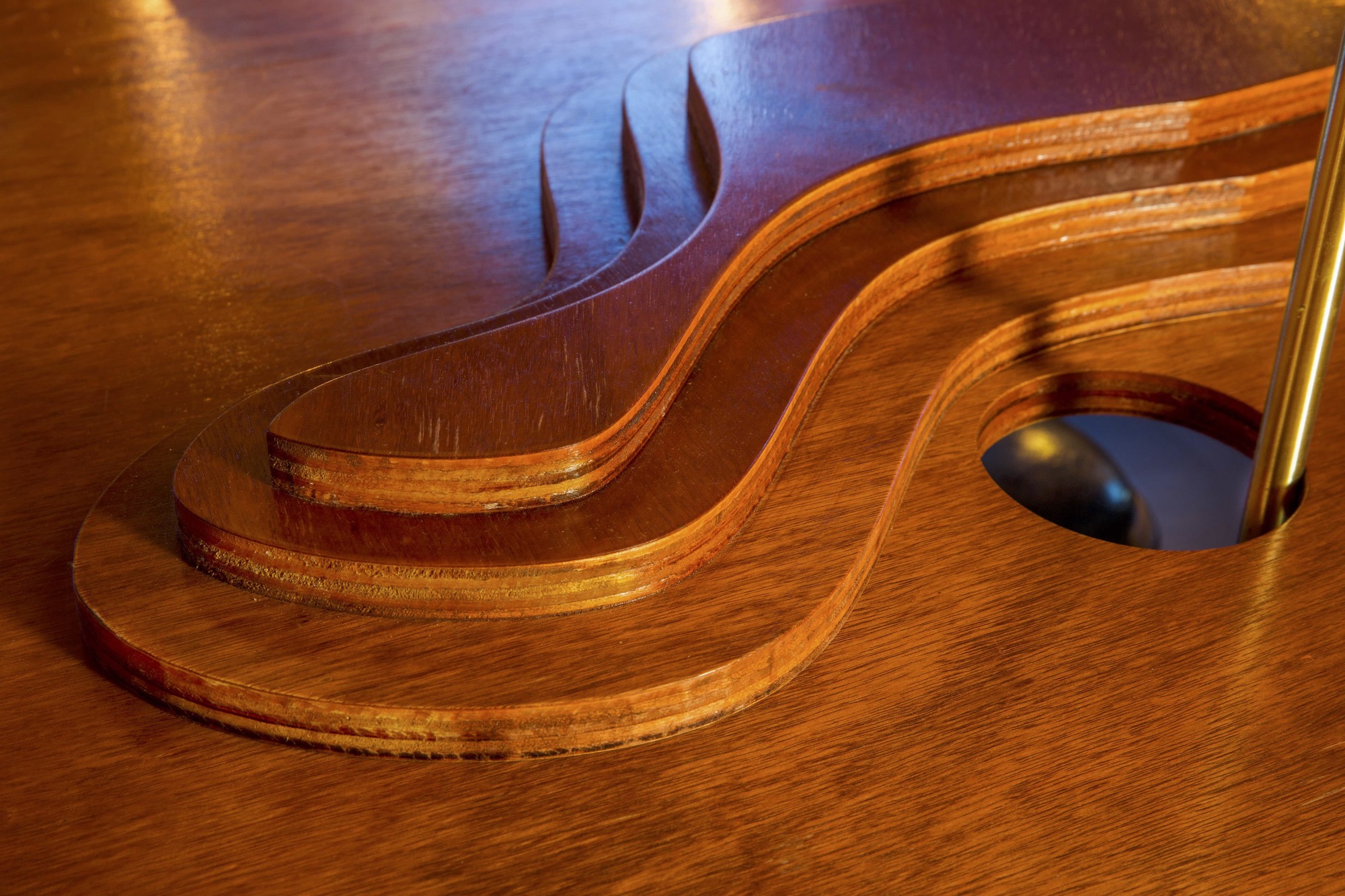 Close-up of layered plywood table edge with flame-shaped cutout against the timber floor