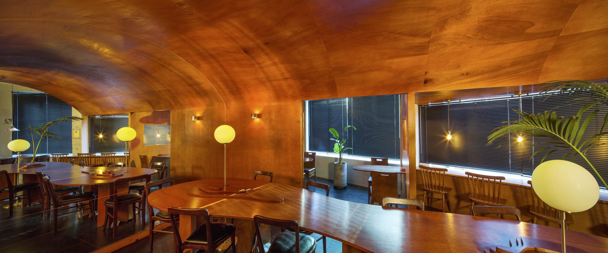 Wide view of the dining hall showing the vaulted timber ceiling and window bays at evening