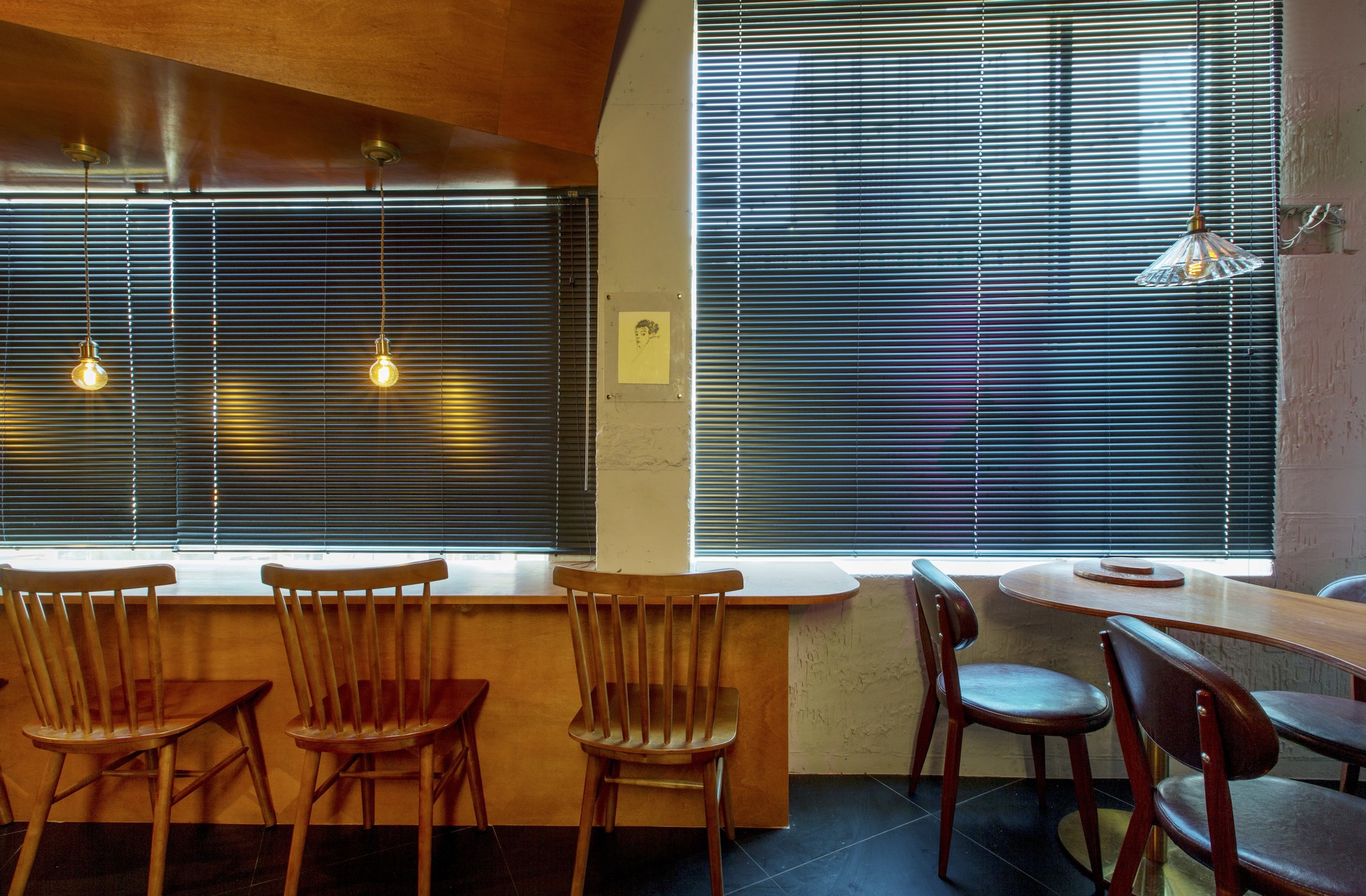Seating alcove with horizontal blinds and wooden chairs arranged along a curved bar counter