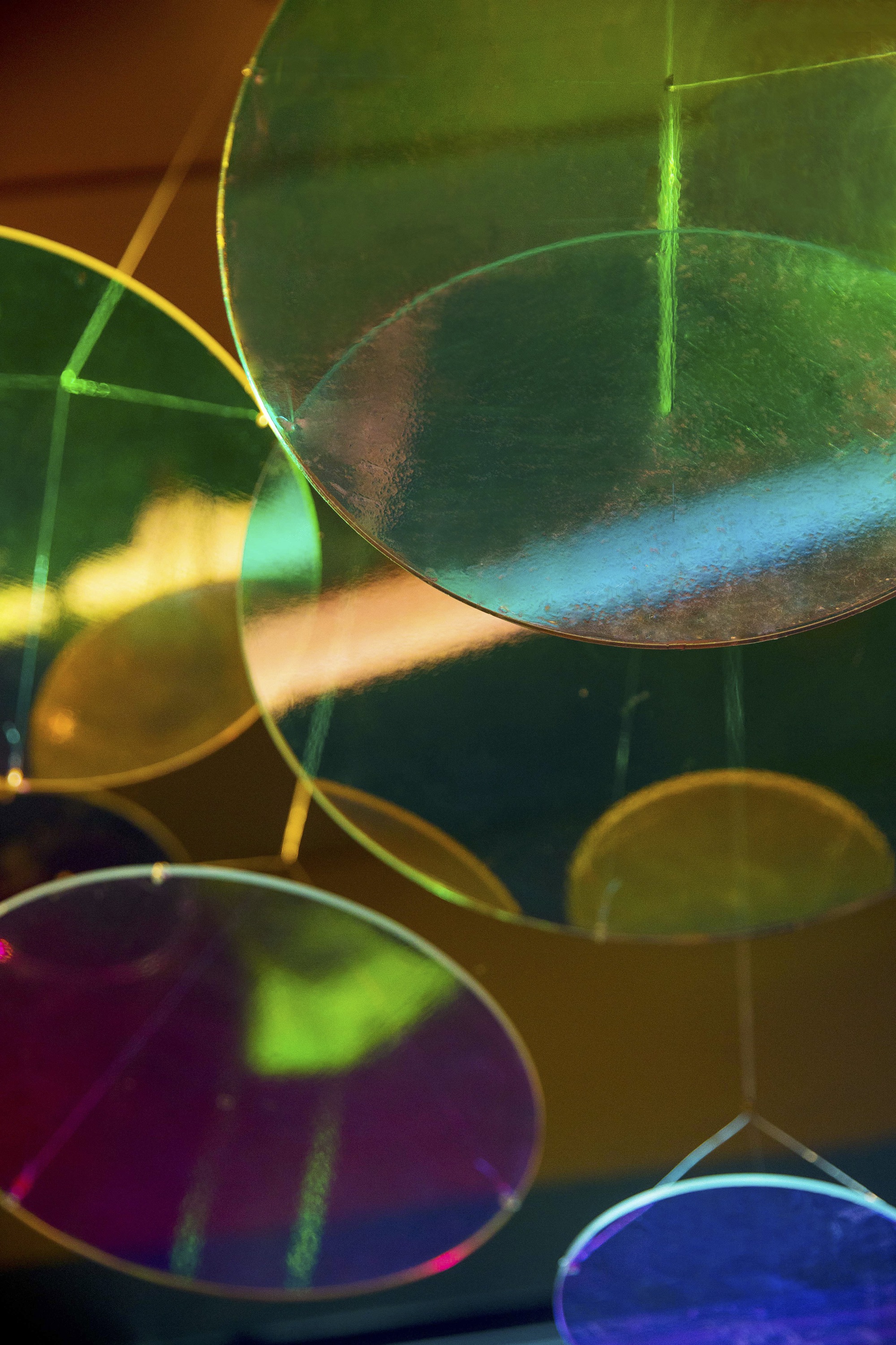 Close-up of overlapping translucent colored glass discs casting layered green, purple, and amber light reflections