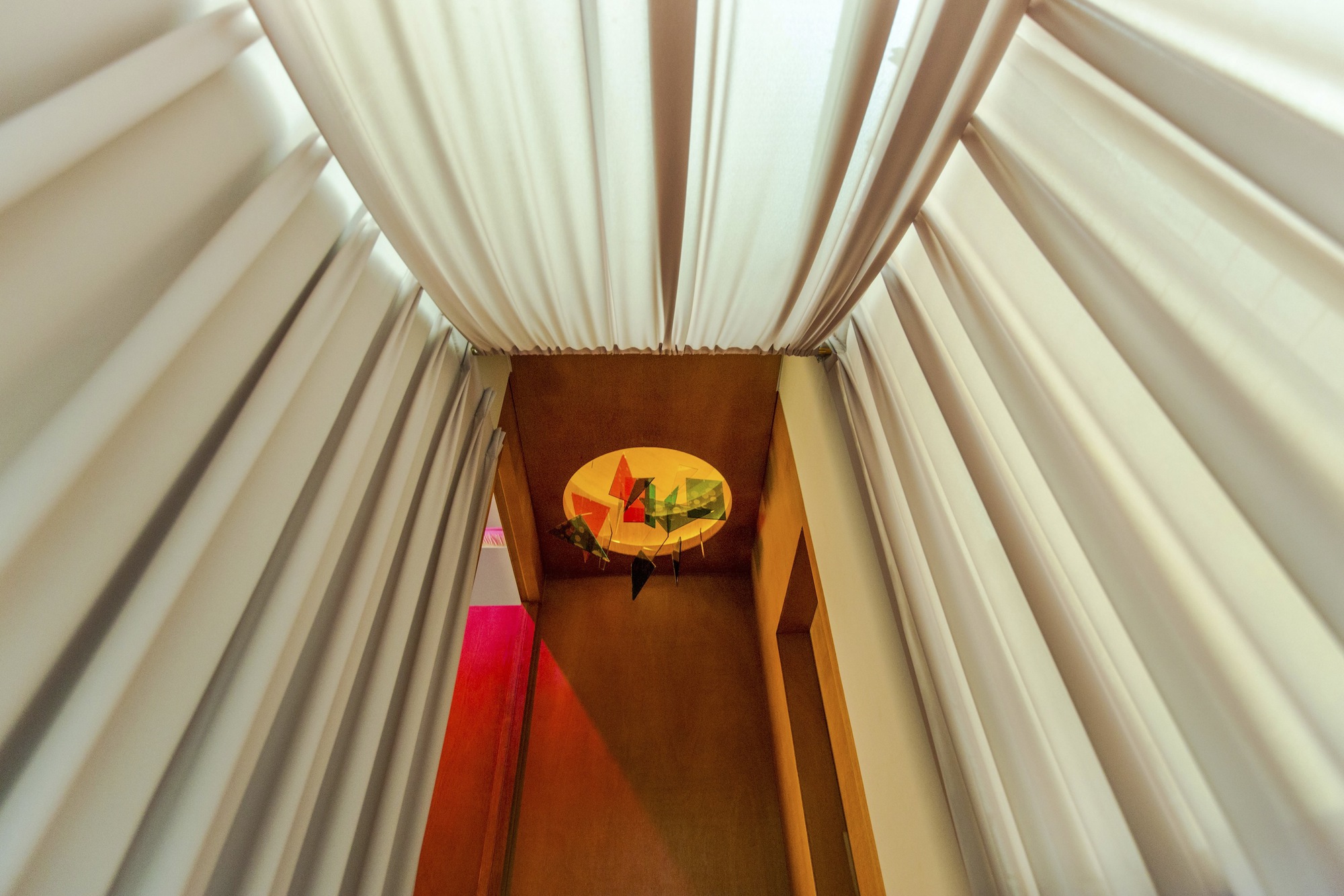Overhead view down a narrow stairwell with white pleated fabric walls and colored glass disc installation below