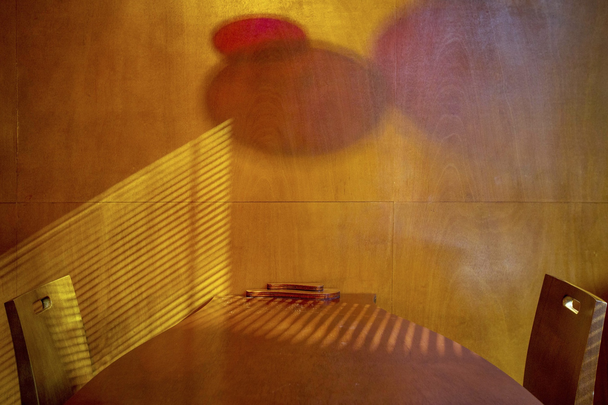 Corner alcove with timber paneling showing striped afternoon sunlight patterns through horizontal blinds and colored light shadow above