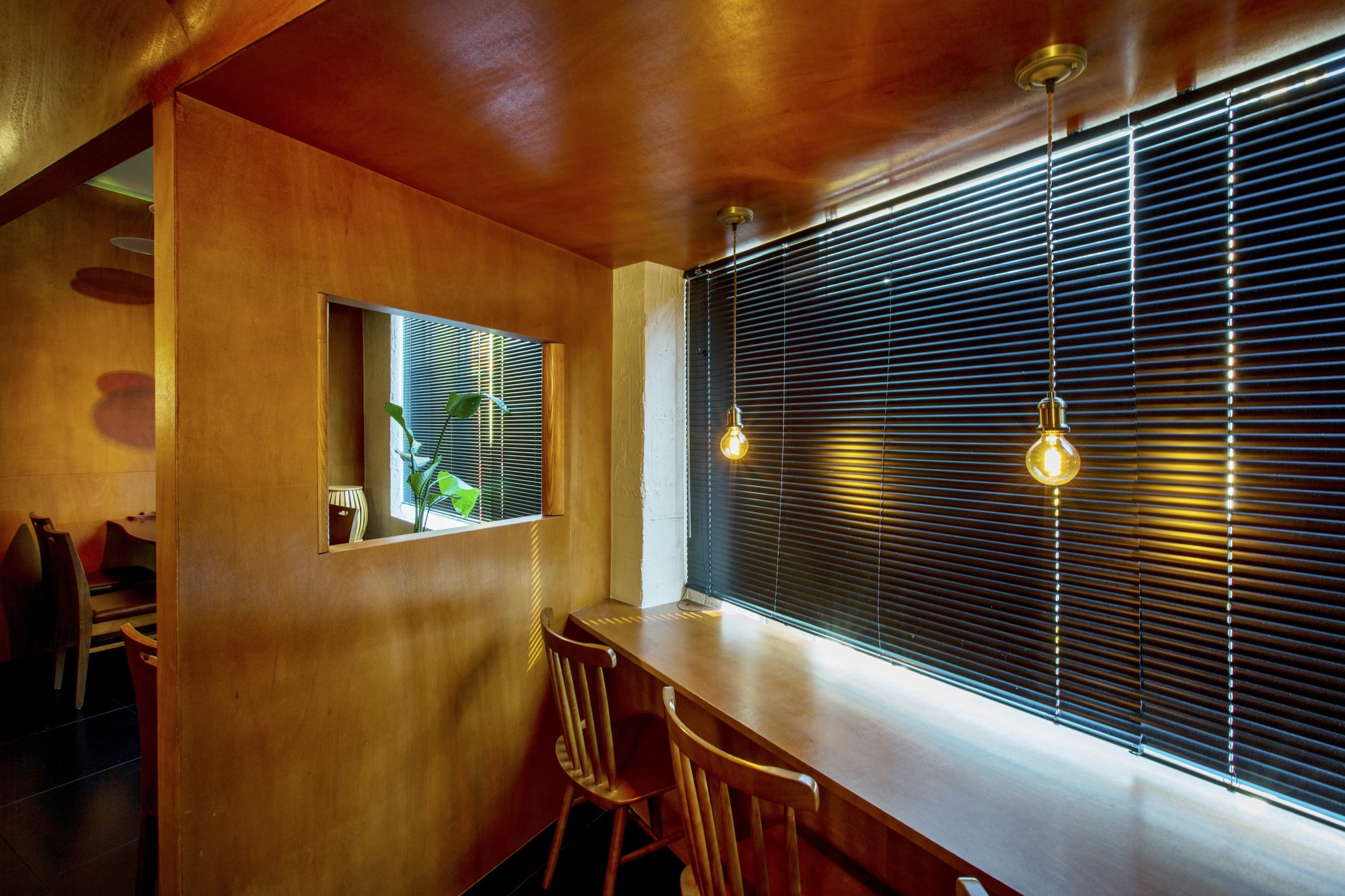 Dining counter with plywood partition and black horizontal blinds lit by pendant bulbs at dusk