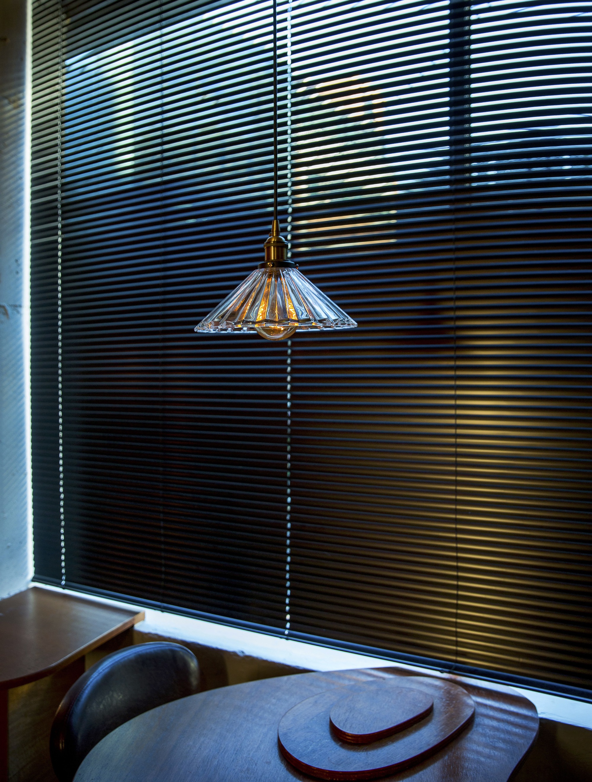Ribbed glass pendant lamp hanging before black metal blinds with afternoon light filtering through