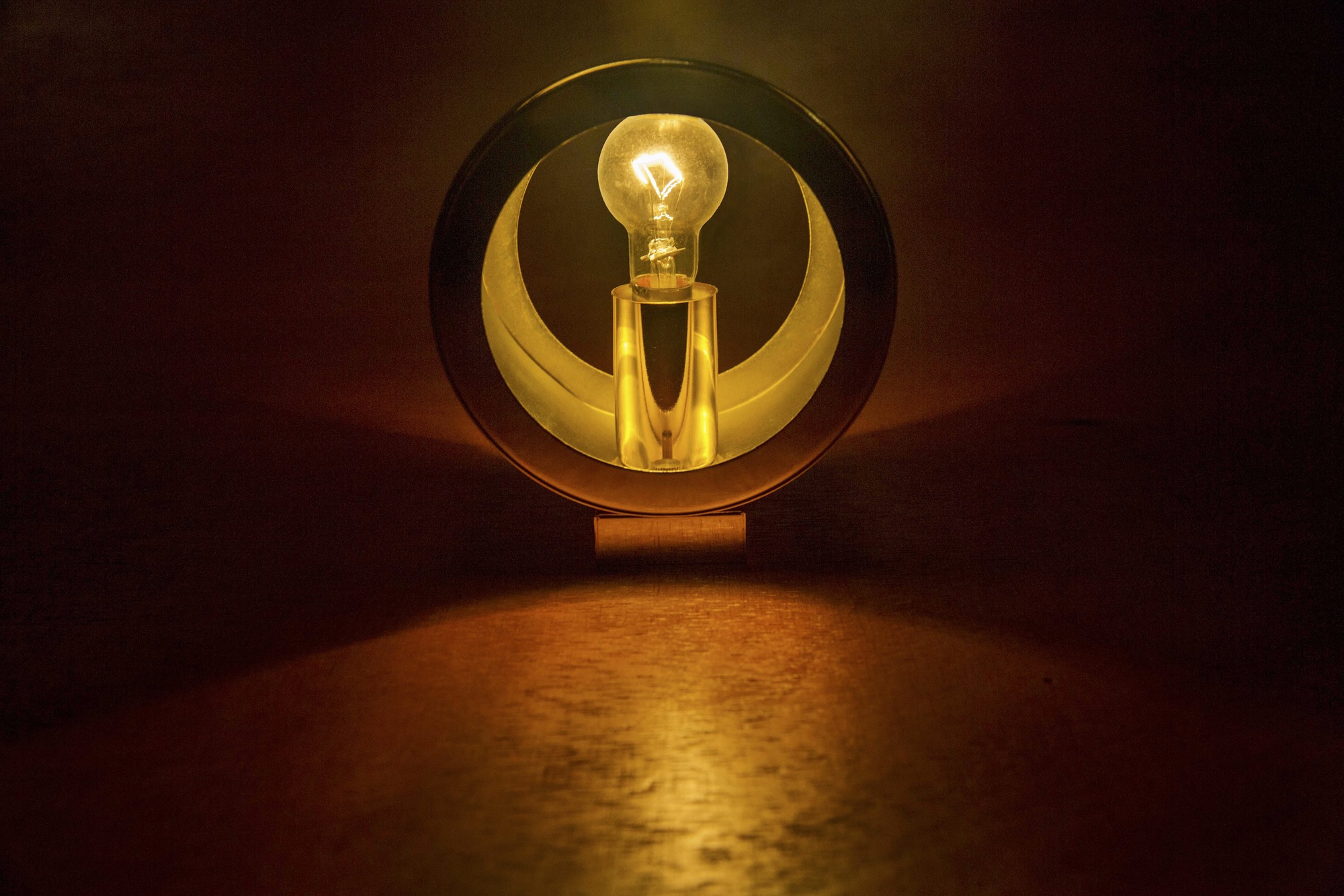 Circular brass portal framing an illuminated bulb above a timber floor in low light