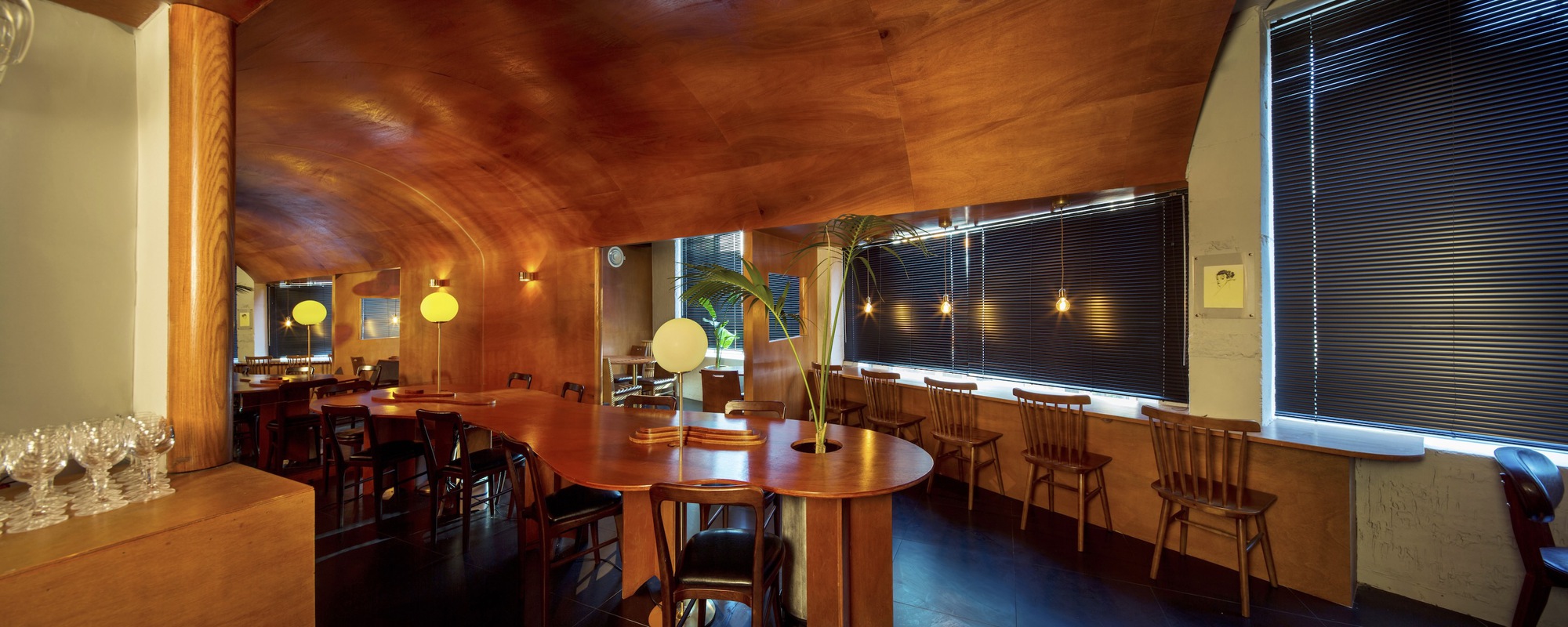 Panoramic view of dining hall with vaulted plywood ceiling and blinds along the window wall