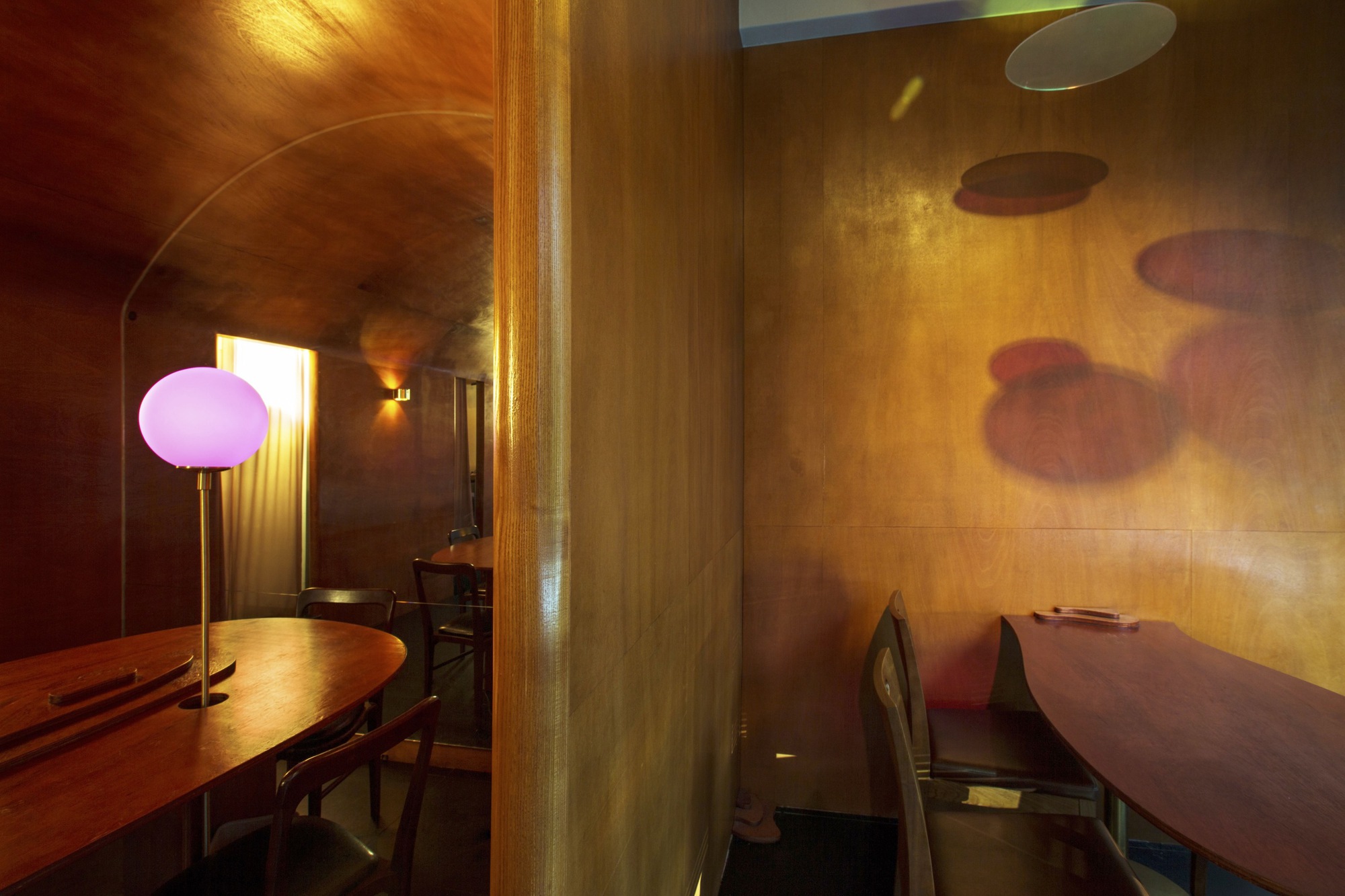 Arched plywood corridor with pink globe lamp and colored shadows cast on the wall