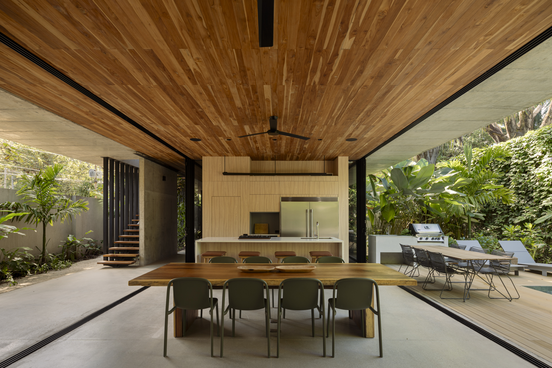 Dining area under timber ceiling with suspended staircase visible through planted courtyard opening