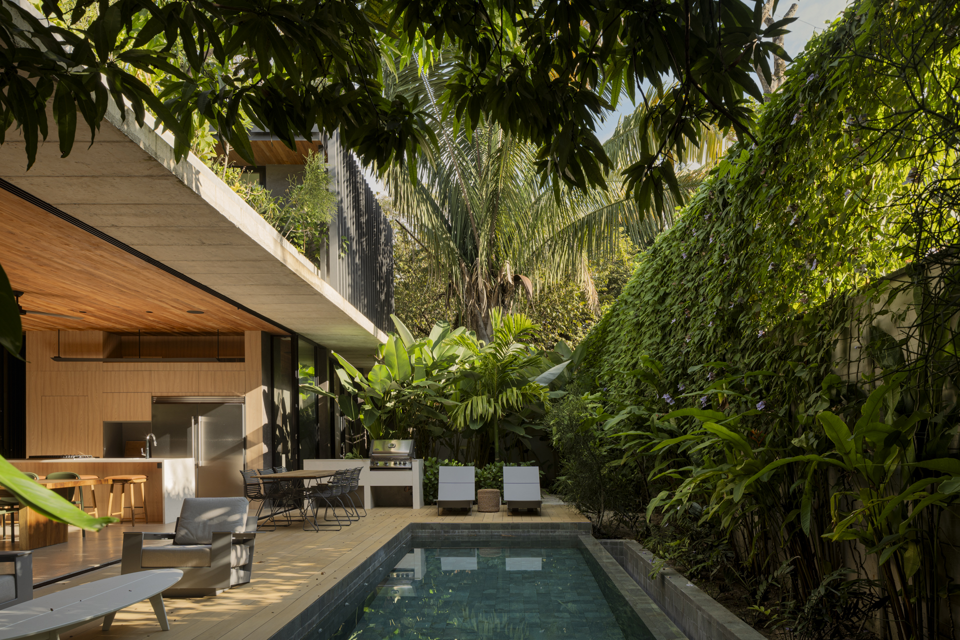 Pool terrace surrounded by dense tropical planting and overhanging concrete roof structure
