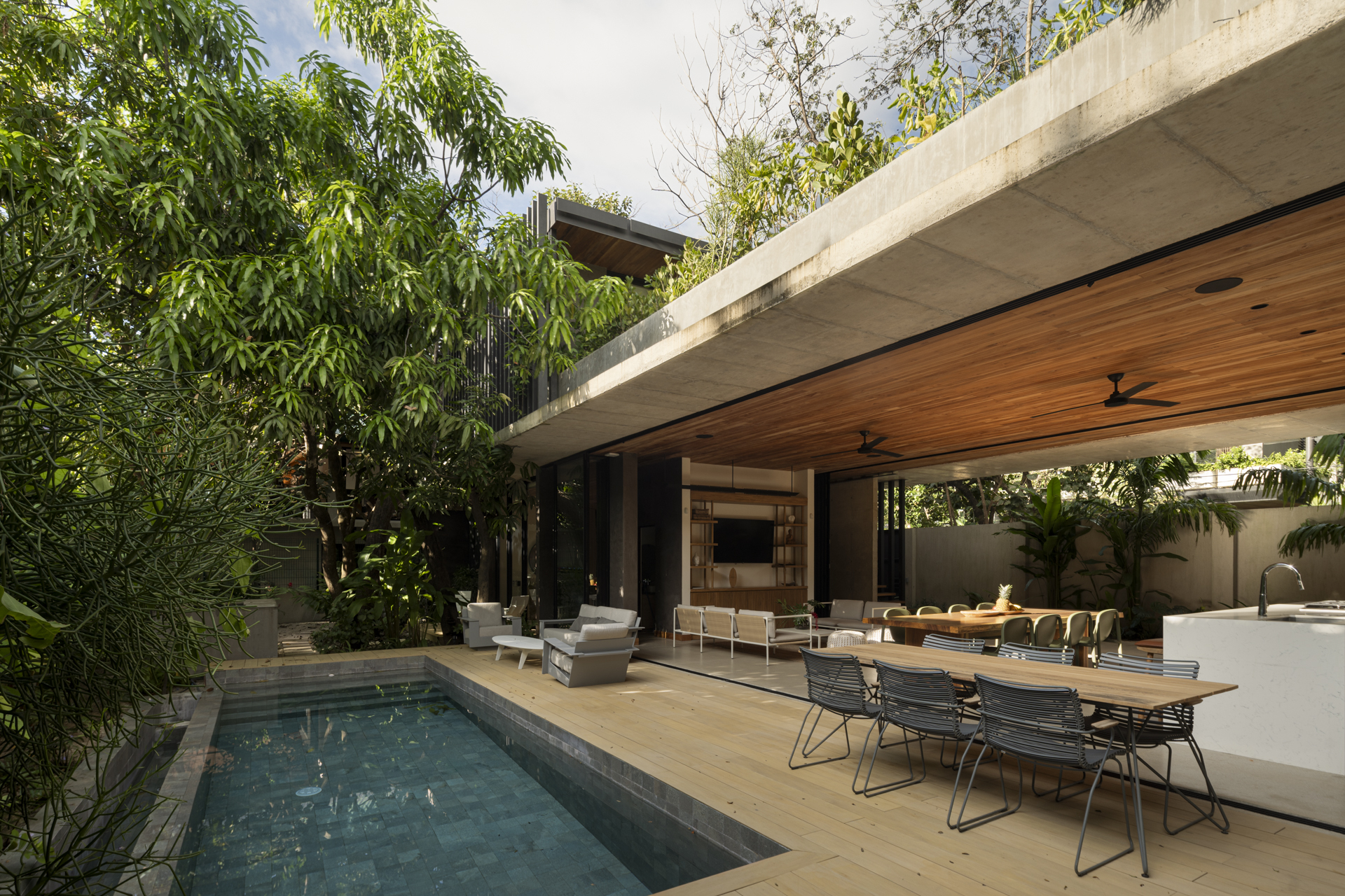 Outdoor dining area beside pool with cantilevered concrete roof and timber ceiling soffit