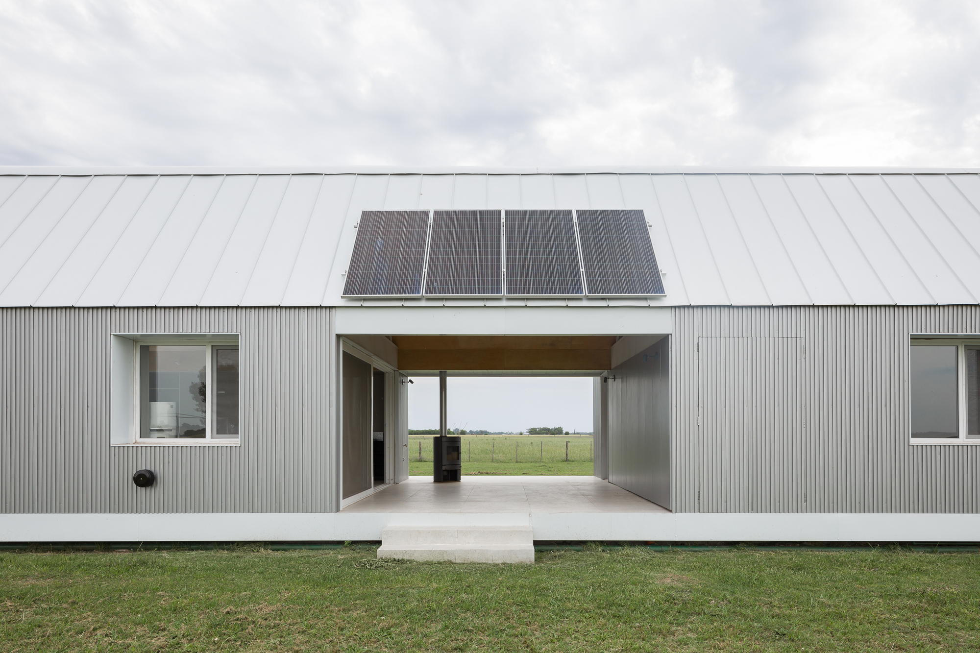 Corrugated metal facade with central breezeway passage and solar panels on the gabled roof