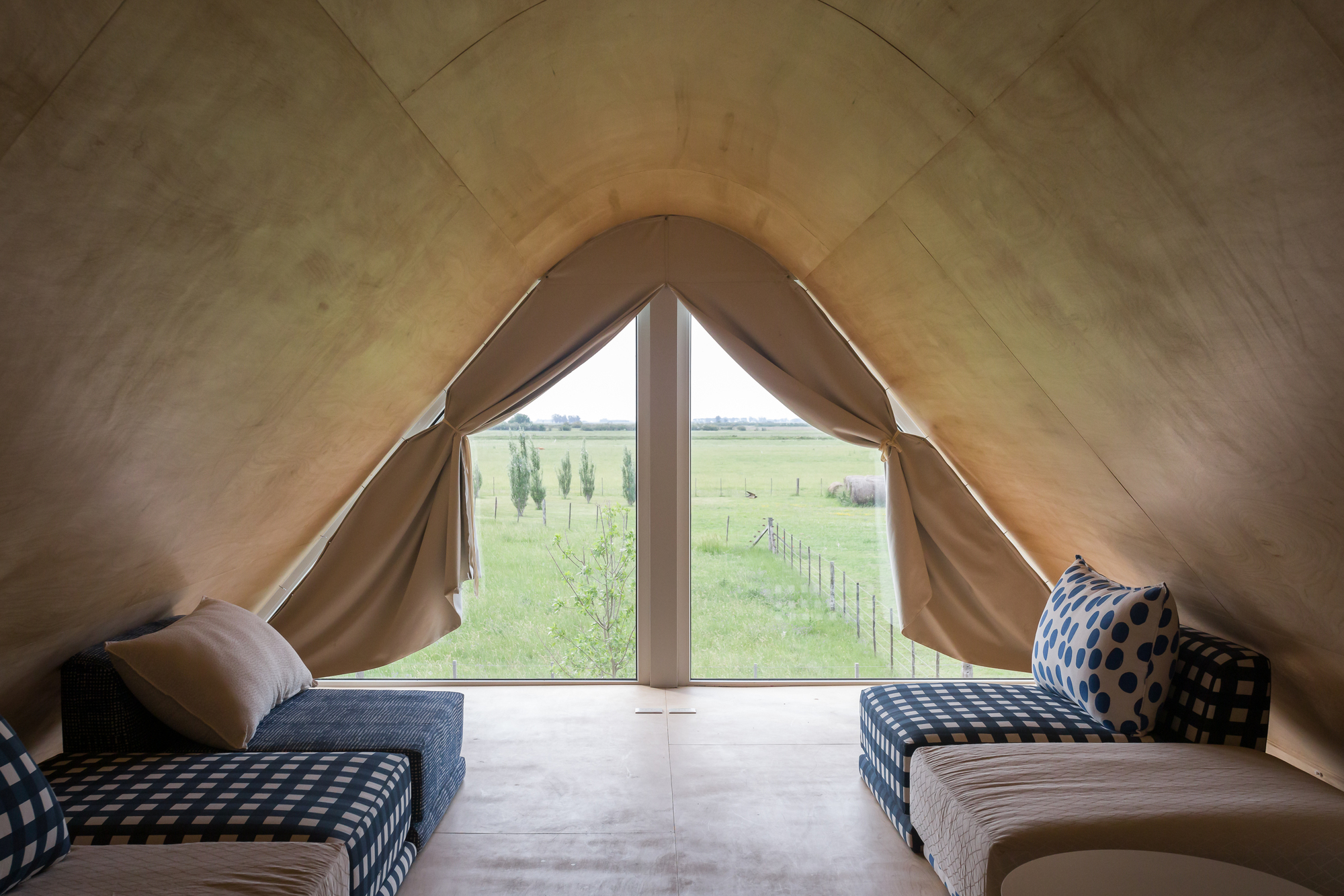 Interior view of plywood-lined gable ceiling with pointed window overlooking open farmland