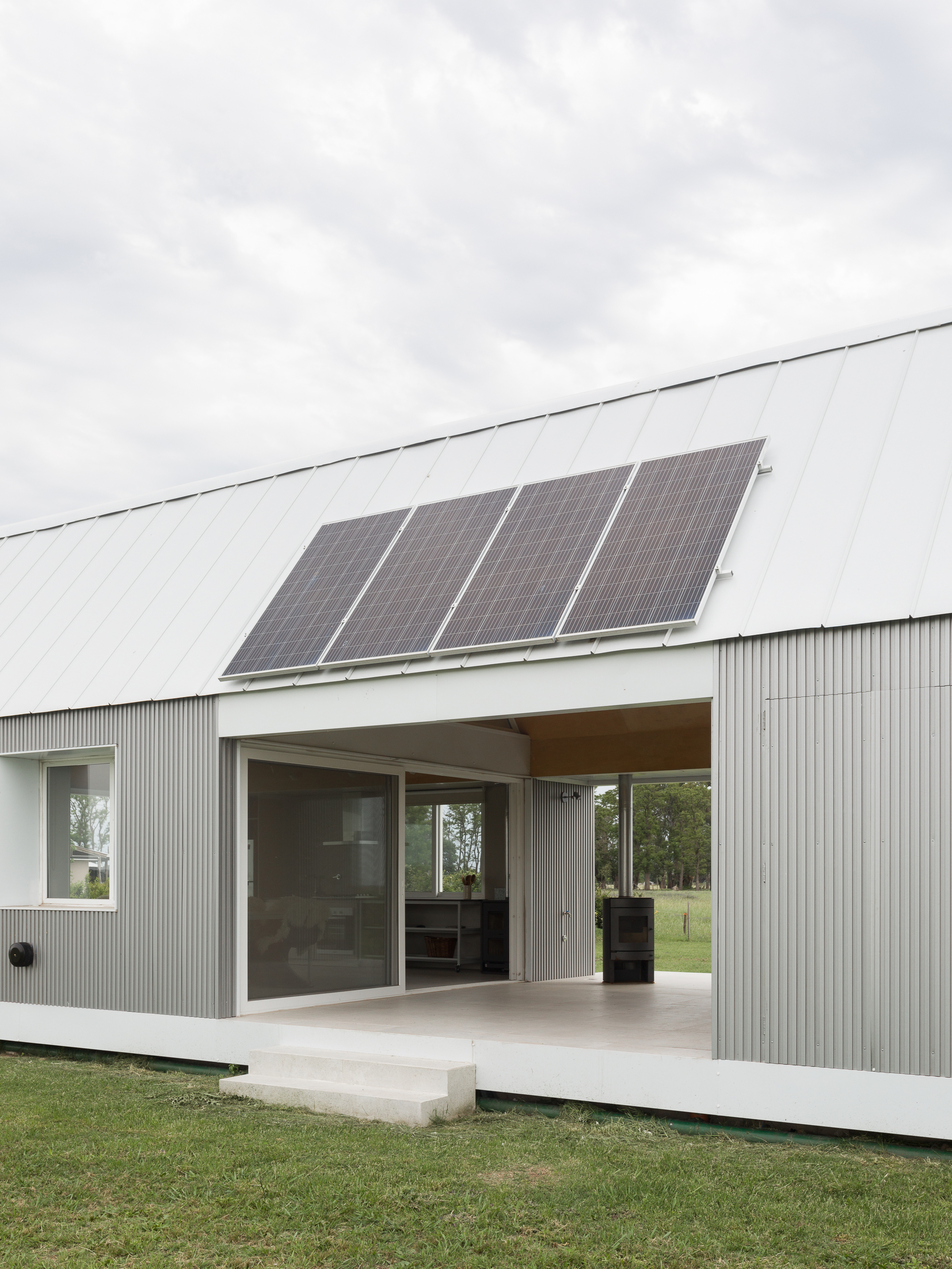 Concrete terrace and sliding doors beneath metal roof with four mounted solar panels