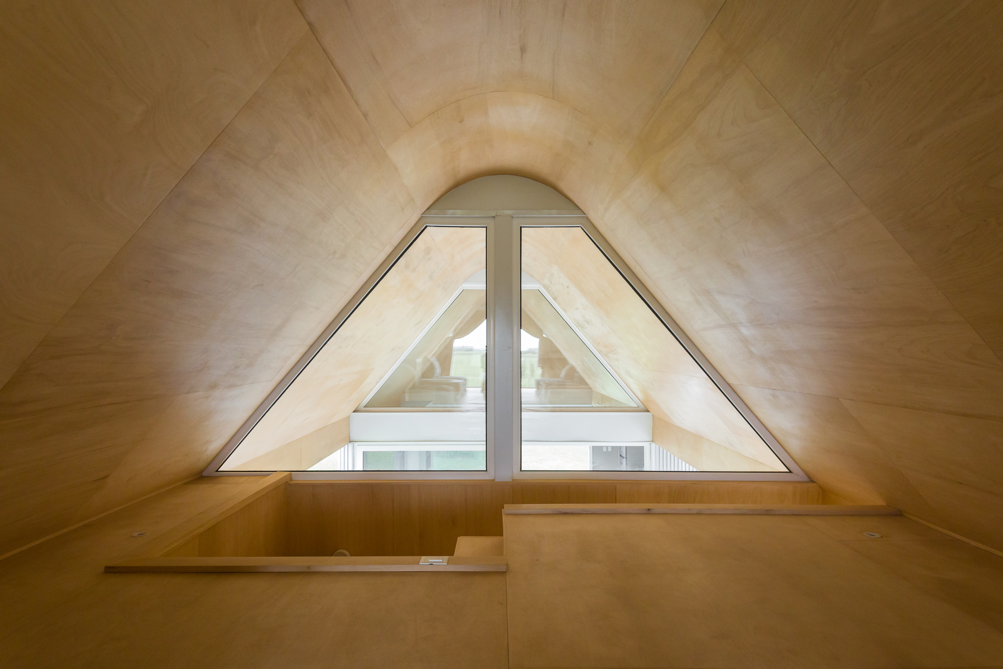 Arched triangular window set in a plywood-clad gable with a built-in bench below