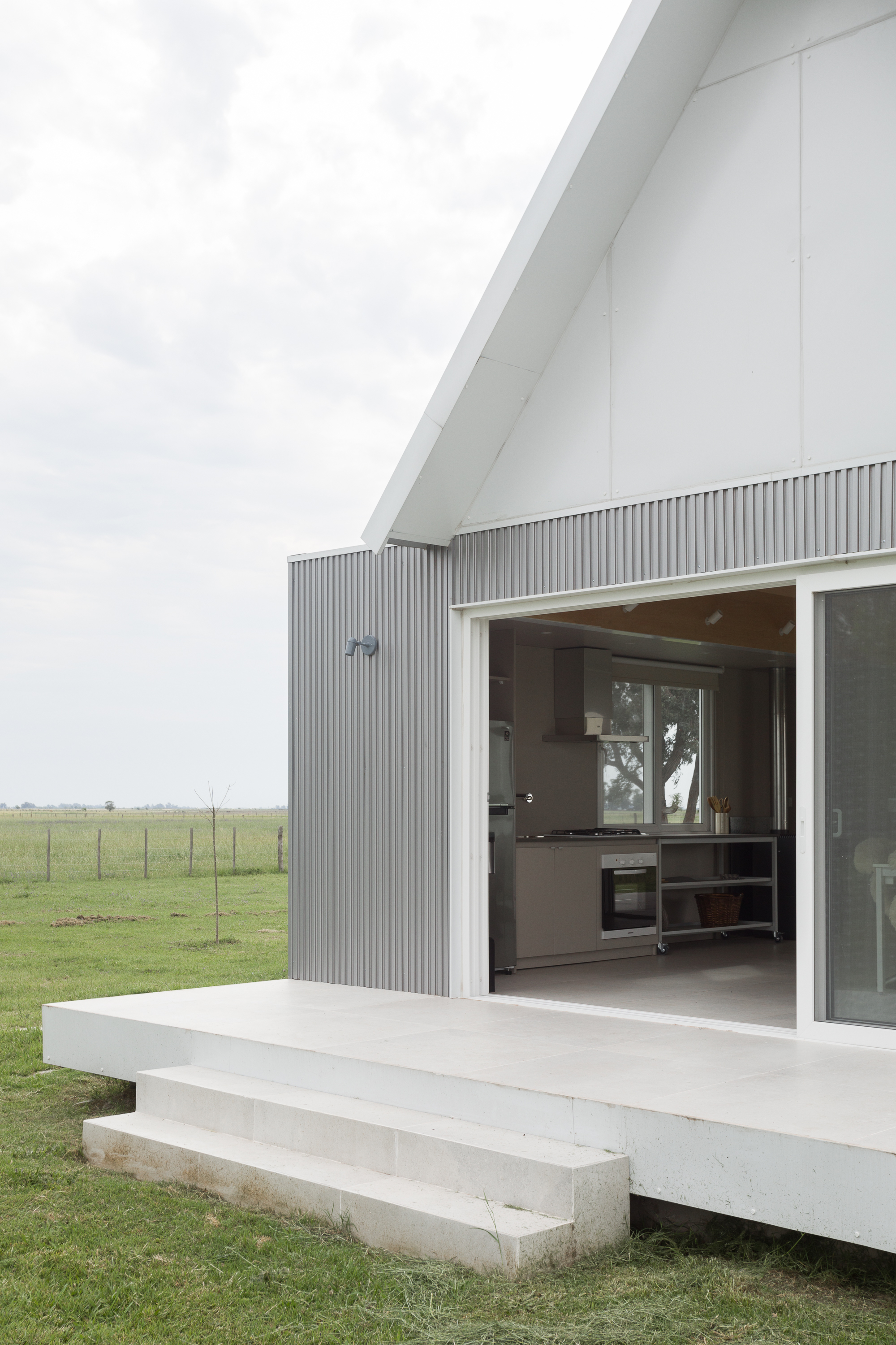Open glass sliding doors revealing a kitchen inside, with a white terrace and concrete steps