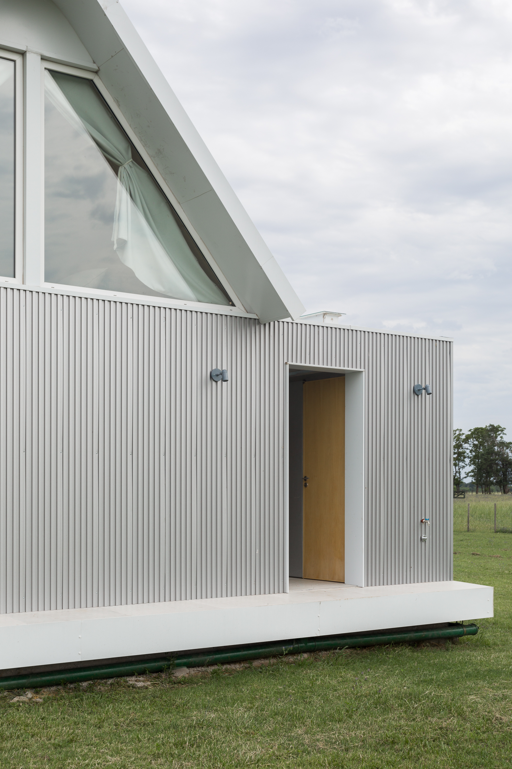 Facade view showing the angled glazed window above the corrugated metal volume on a raised terrace