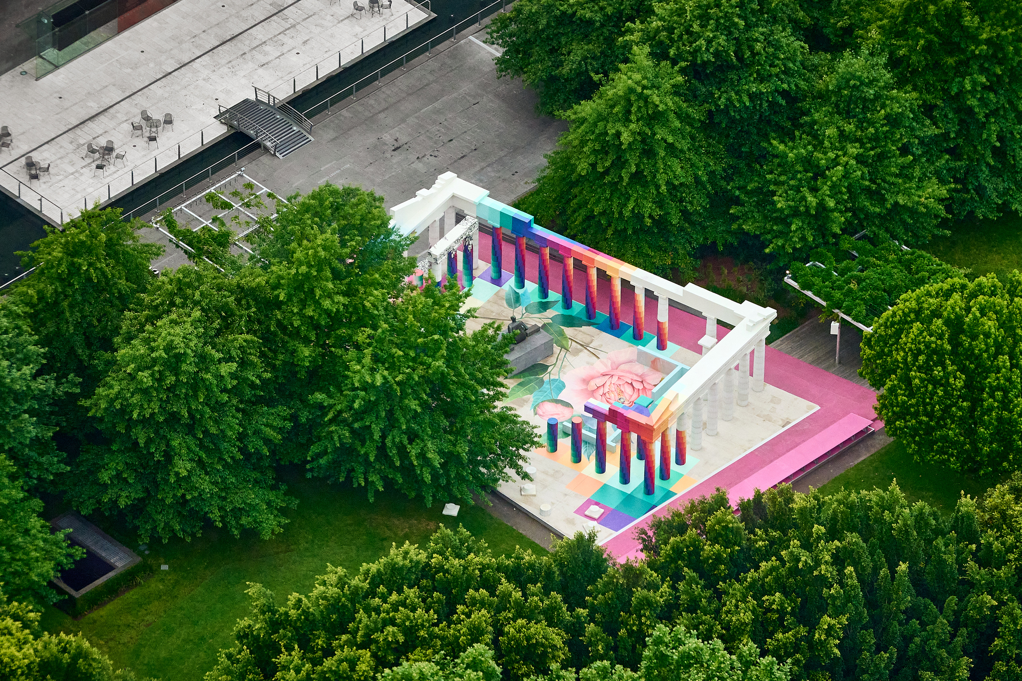 Aerial view of a colonnade with multicolored columns and painted floor murals surrounded by green trees