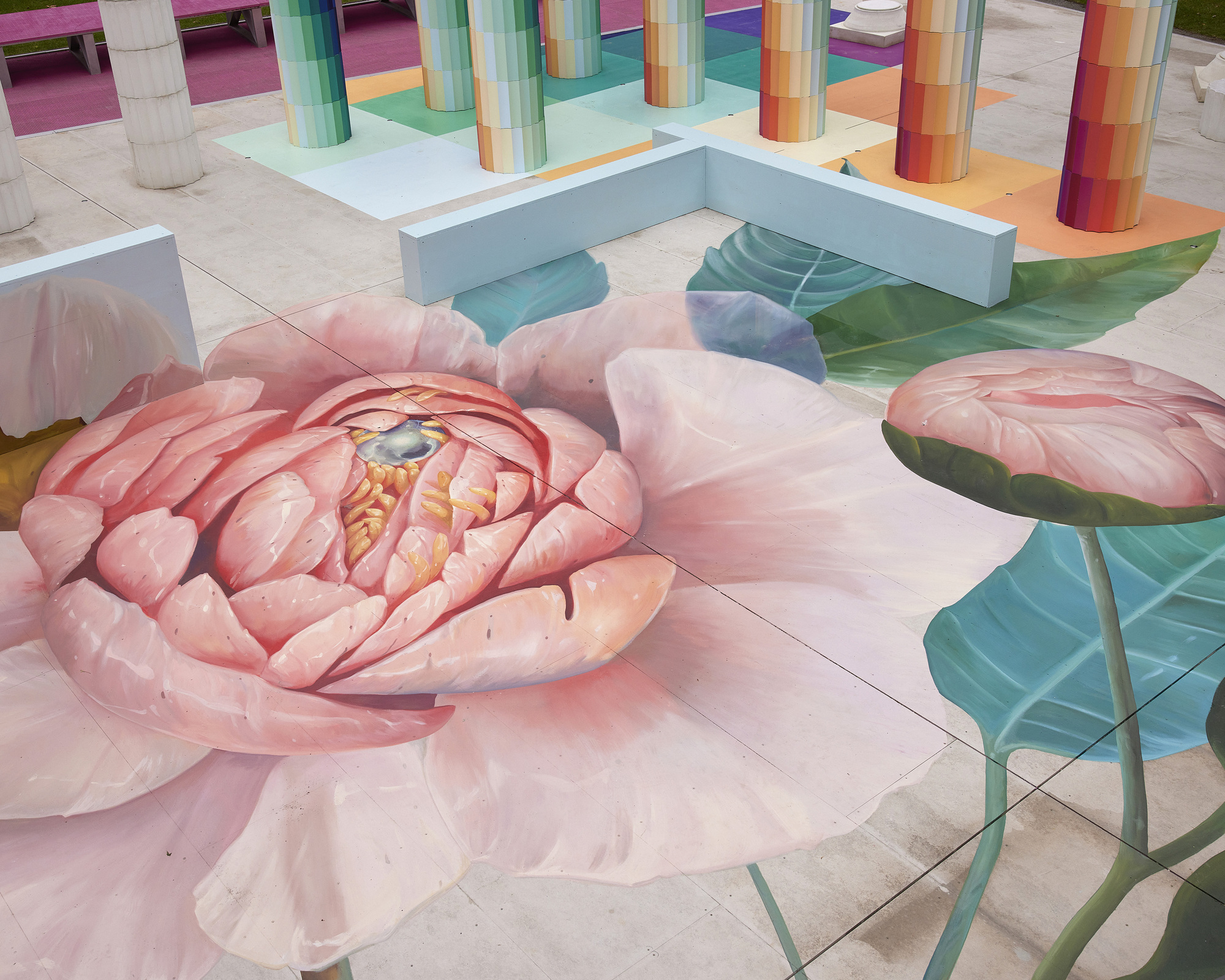 Ground-level view of the floor mural depicting a pink peony blossom with rainbow columns in the background