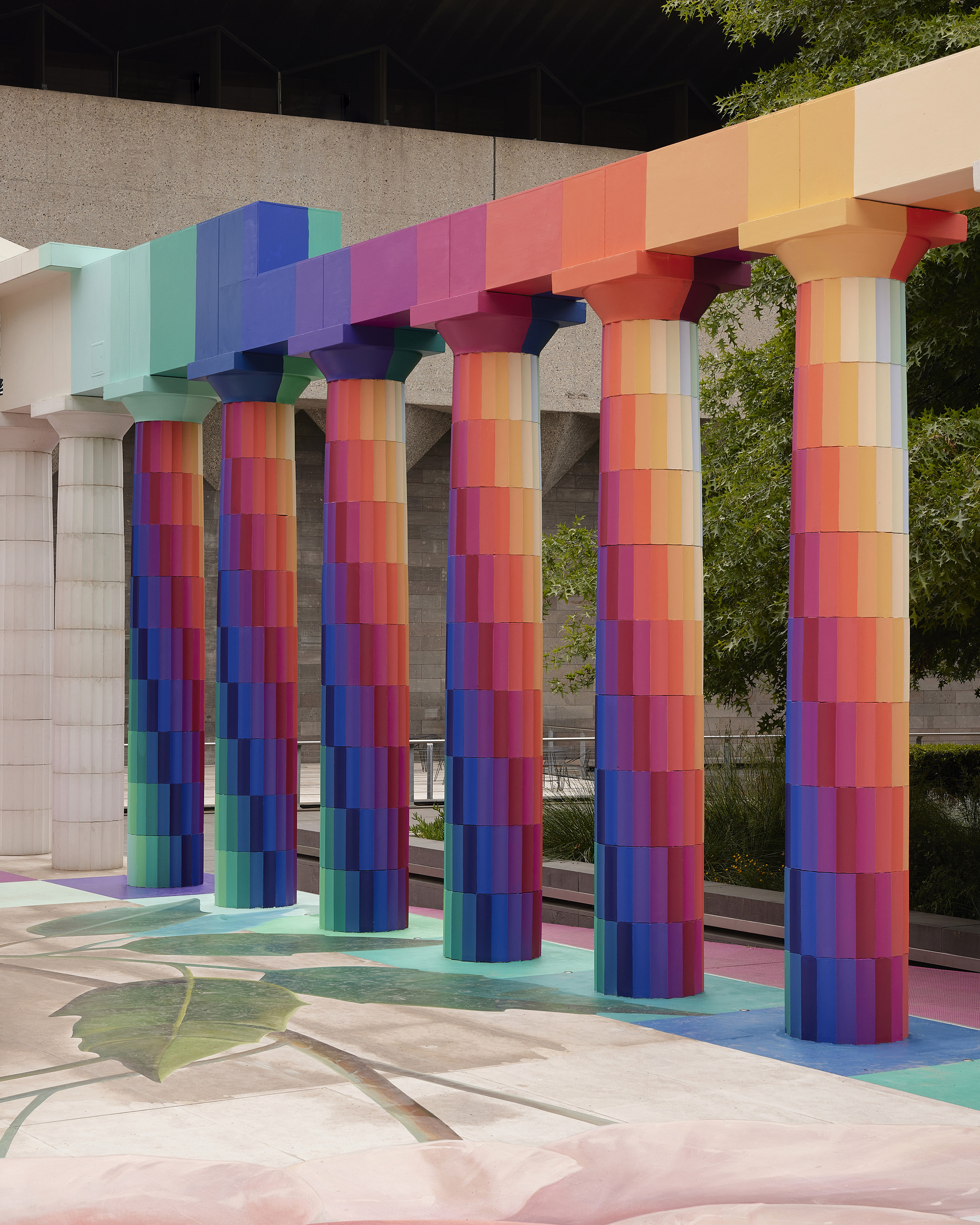 Close-up of the multicolored cylindrical columns supporting the stepped rainbow beam against a concrete backdrop