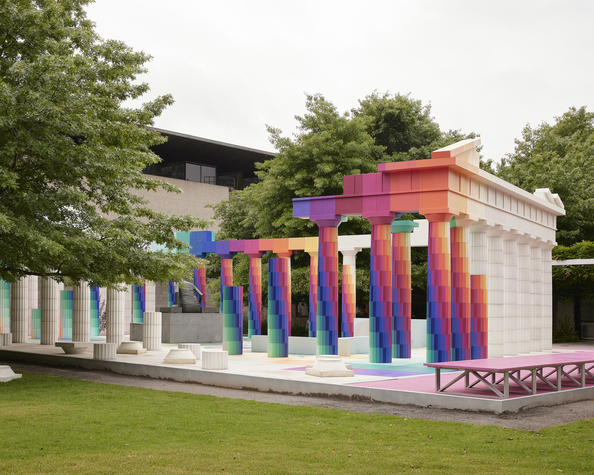 Colonnade structure with multicolored tiled columns and stepped entablature framed by lawn and surrounding greenery