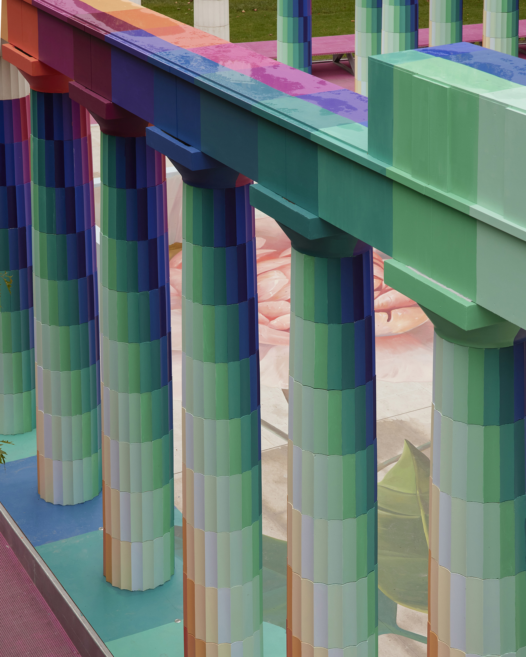 Close-up of pixelated cylindrical columns supporting gradient-striped beams beneath a clear sky
