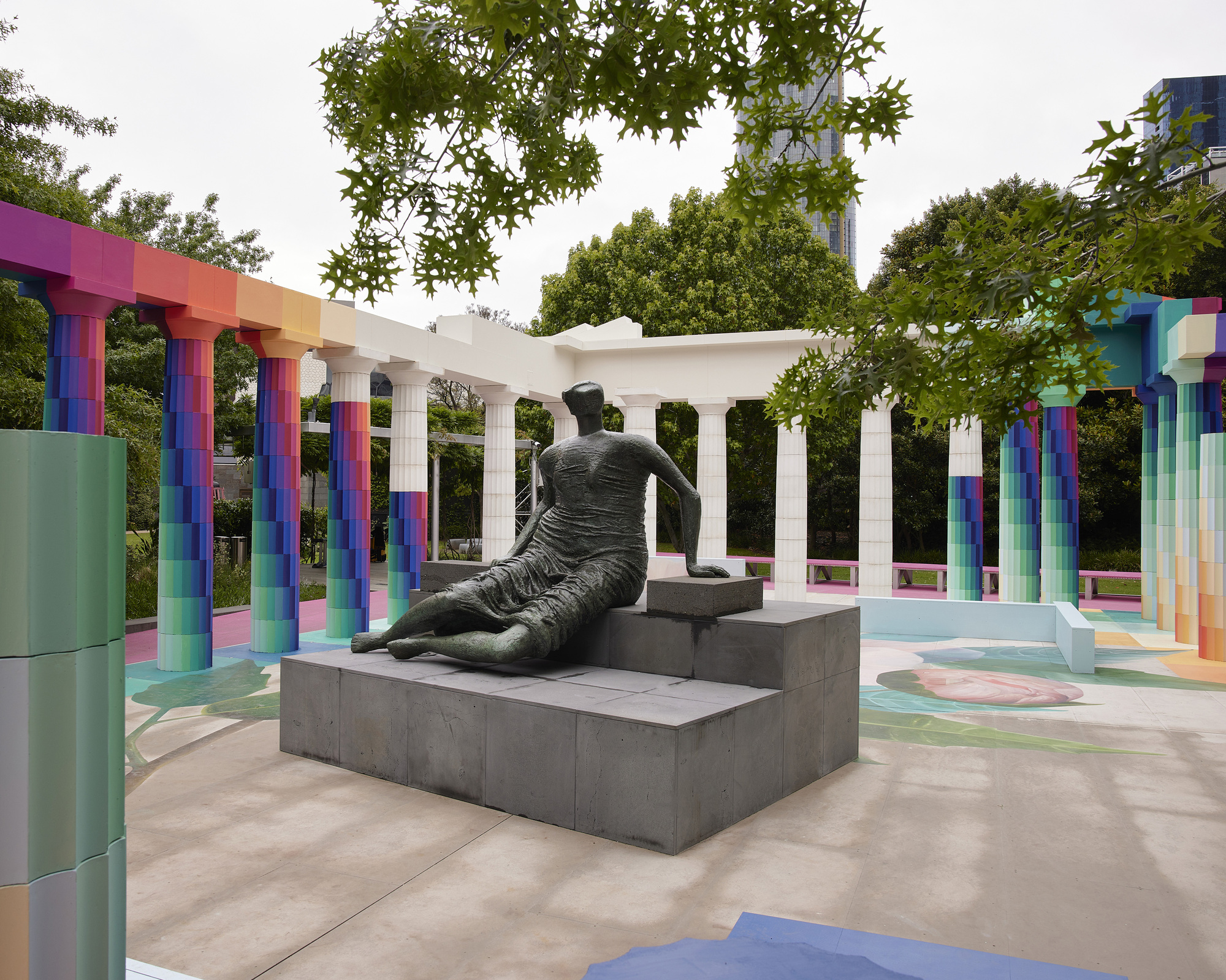 Bronze sculpture on grey plinth surrounded by gradient columns and white entablature on an overcast day