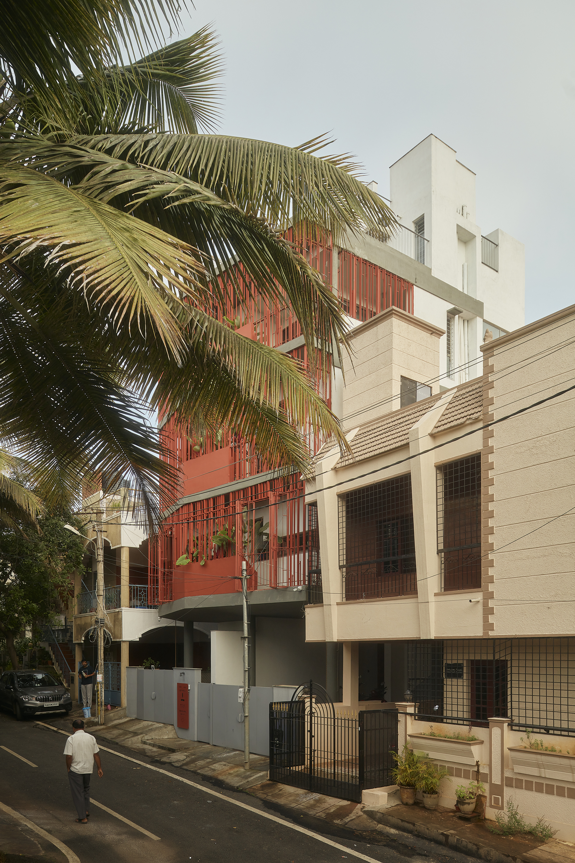 Streetscape view showing the red screened volume rising above neighboring buildings framed by palm fronds