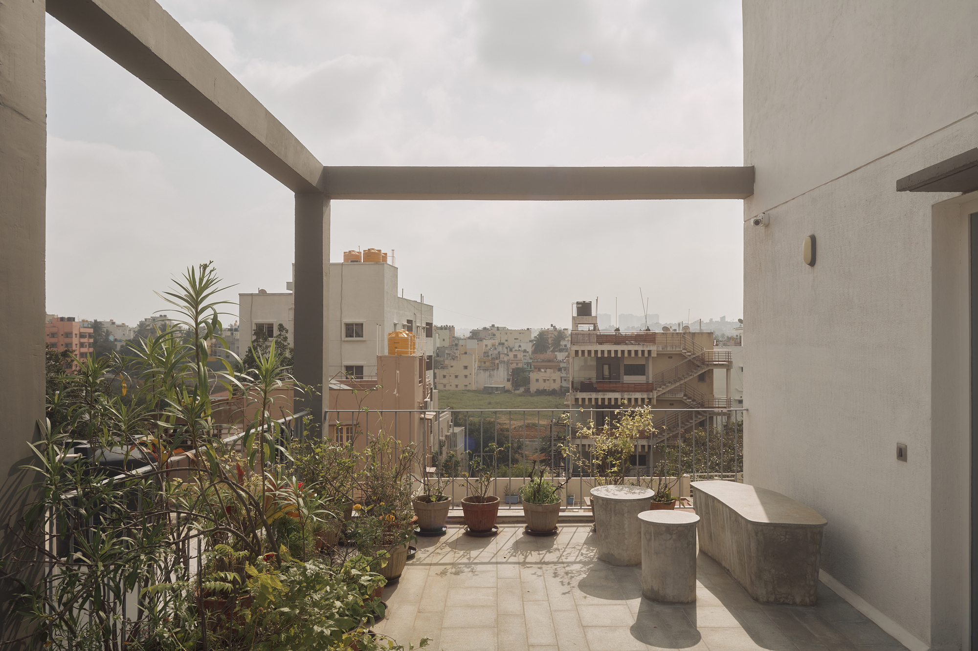 Rooftop terrace with concrete pergola frame overlooking planted pots and the urban skyline beyond