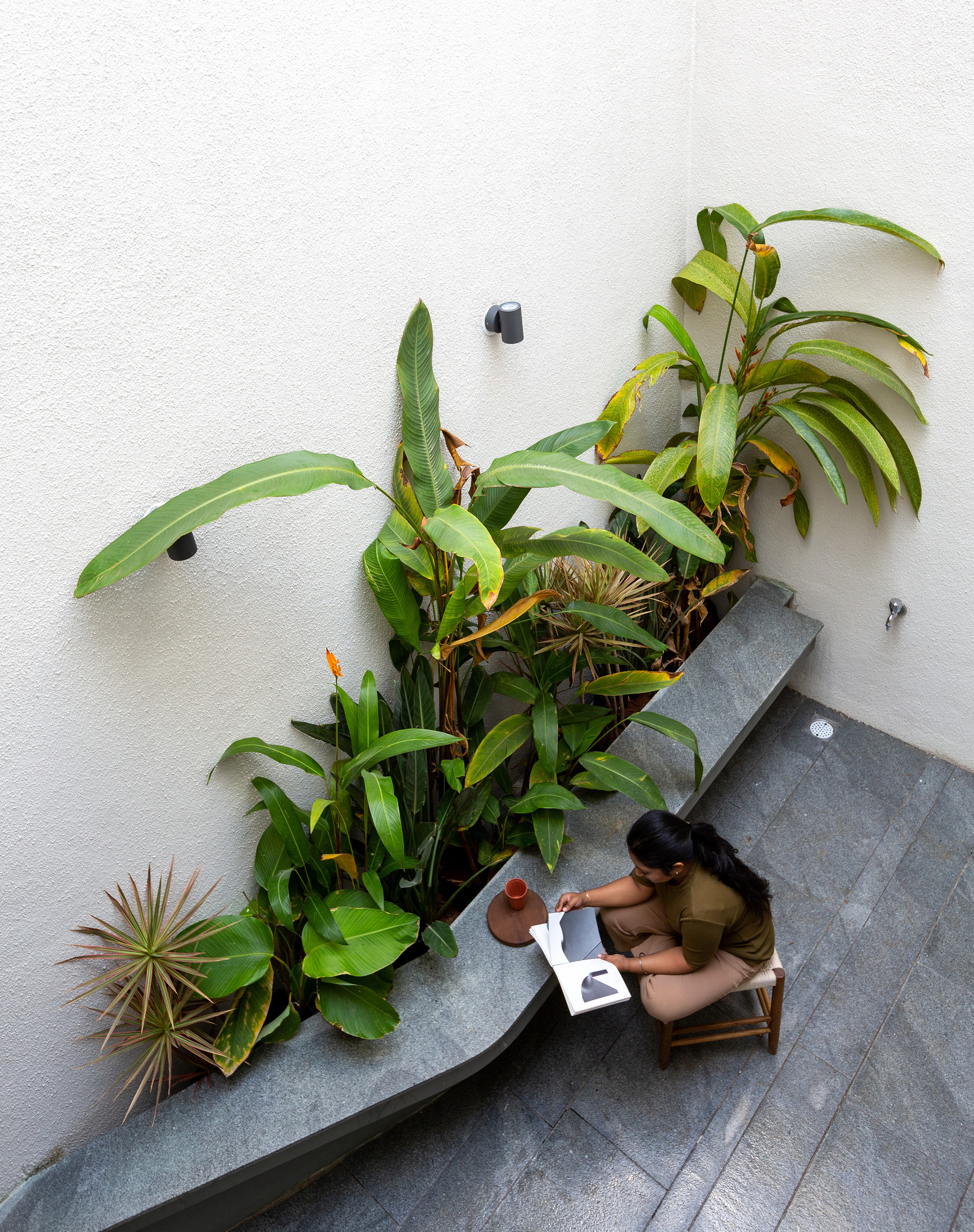 Overhead view of person seated at stone bench beside planted bed in interior courtyard