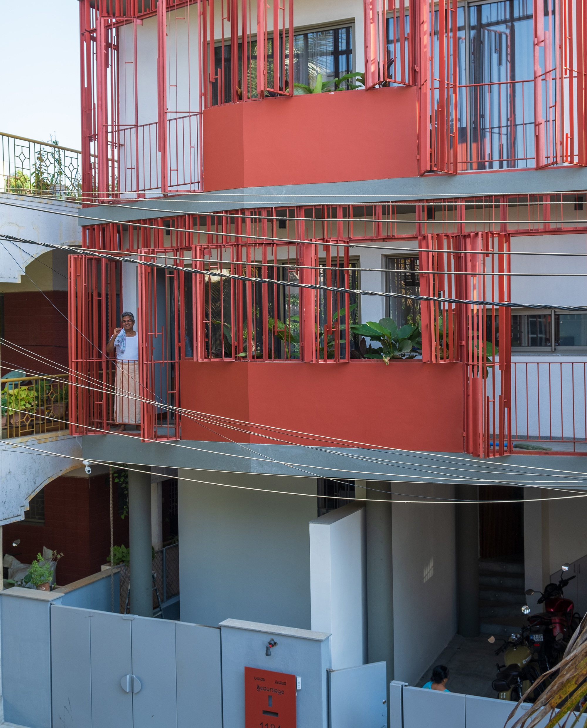 Stacked balconies wrapped in red vertical battens with a resident visible on the upper terrace