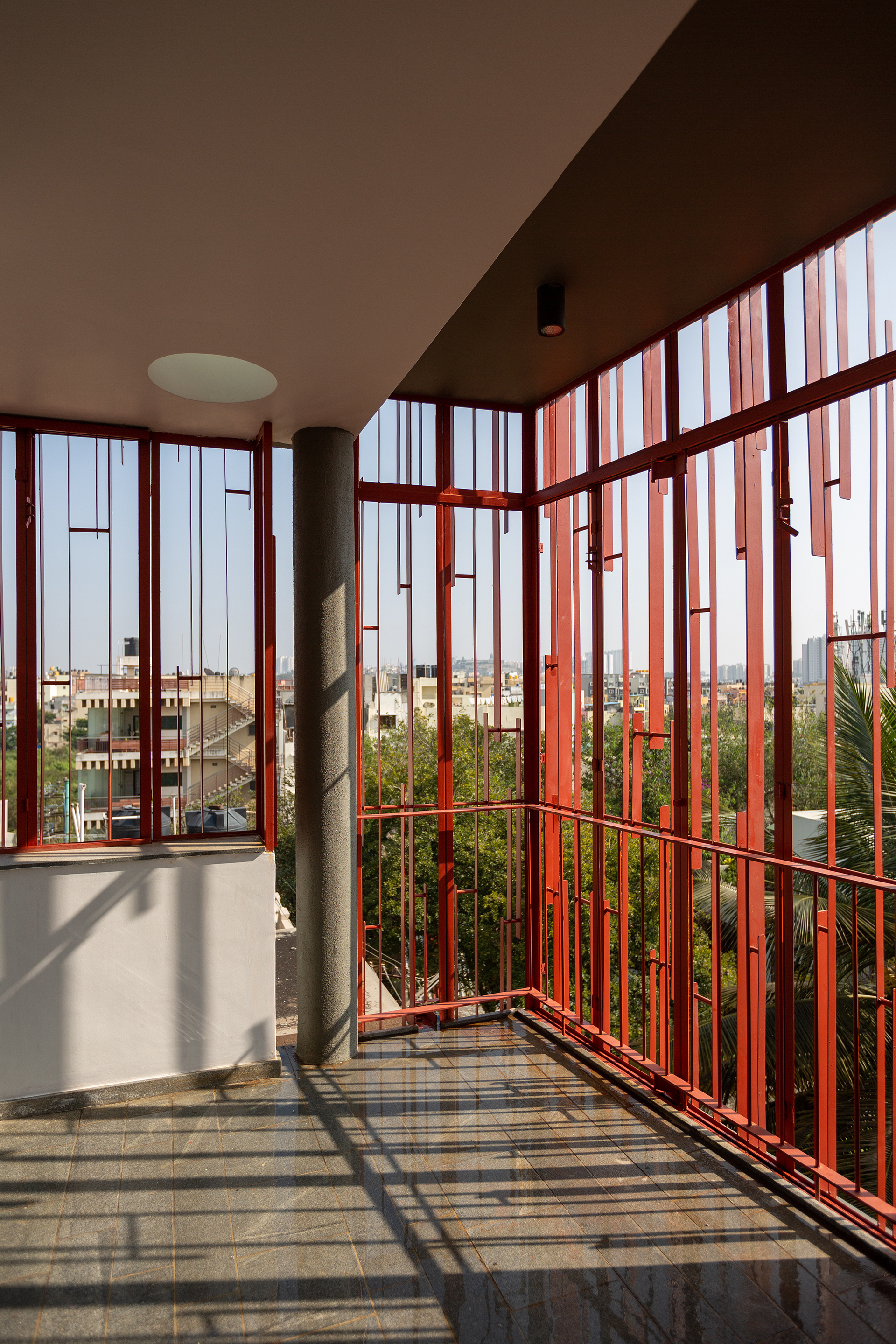 Corner balcony enclosed by red vertical battens casting striped shadows across the tiled floor