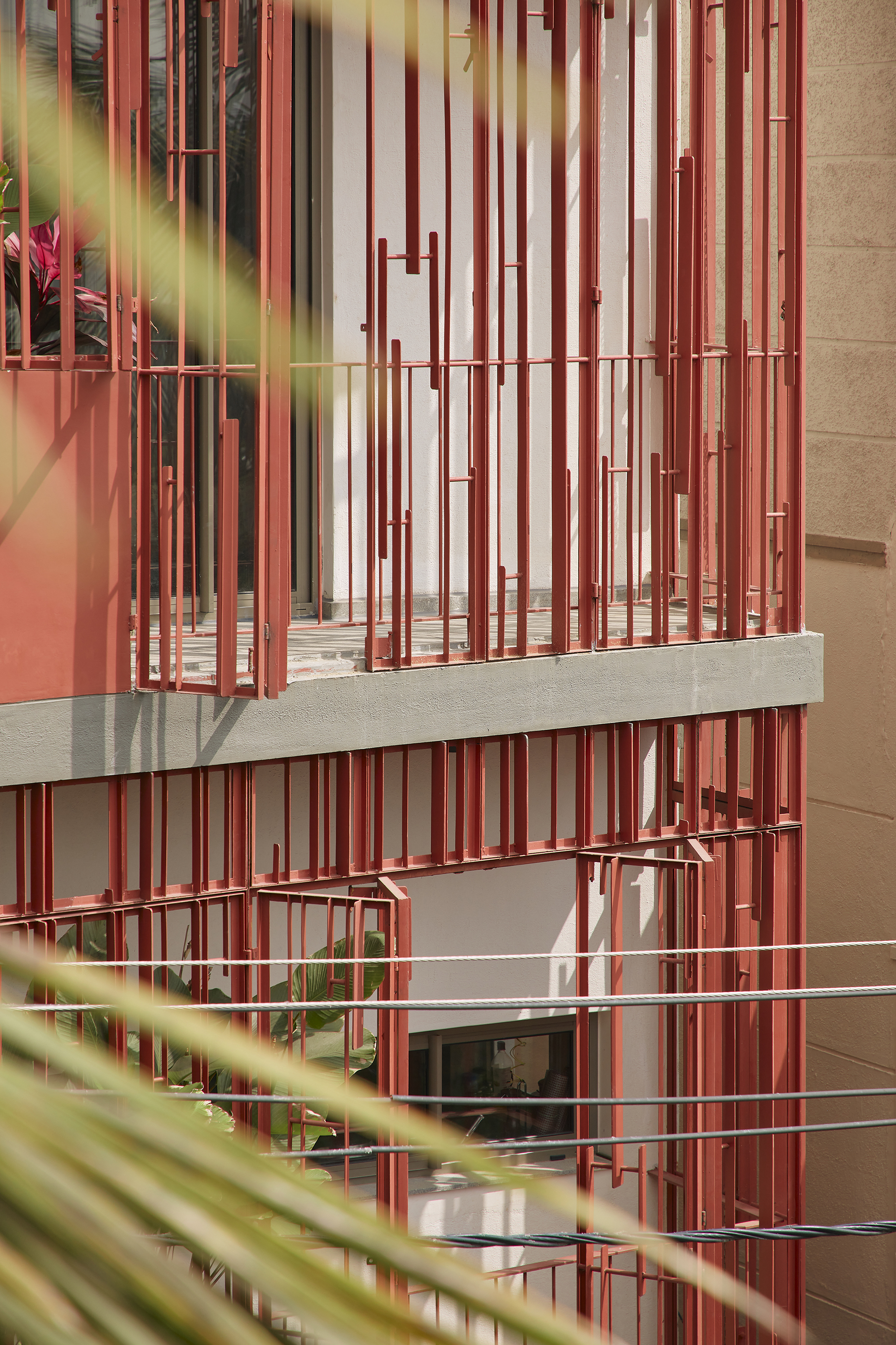 Layered view of red batten screens across multiple levels framed by green foliage