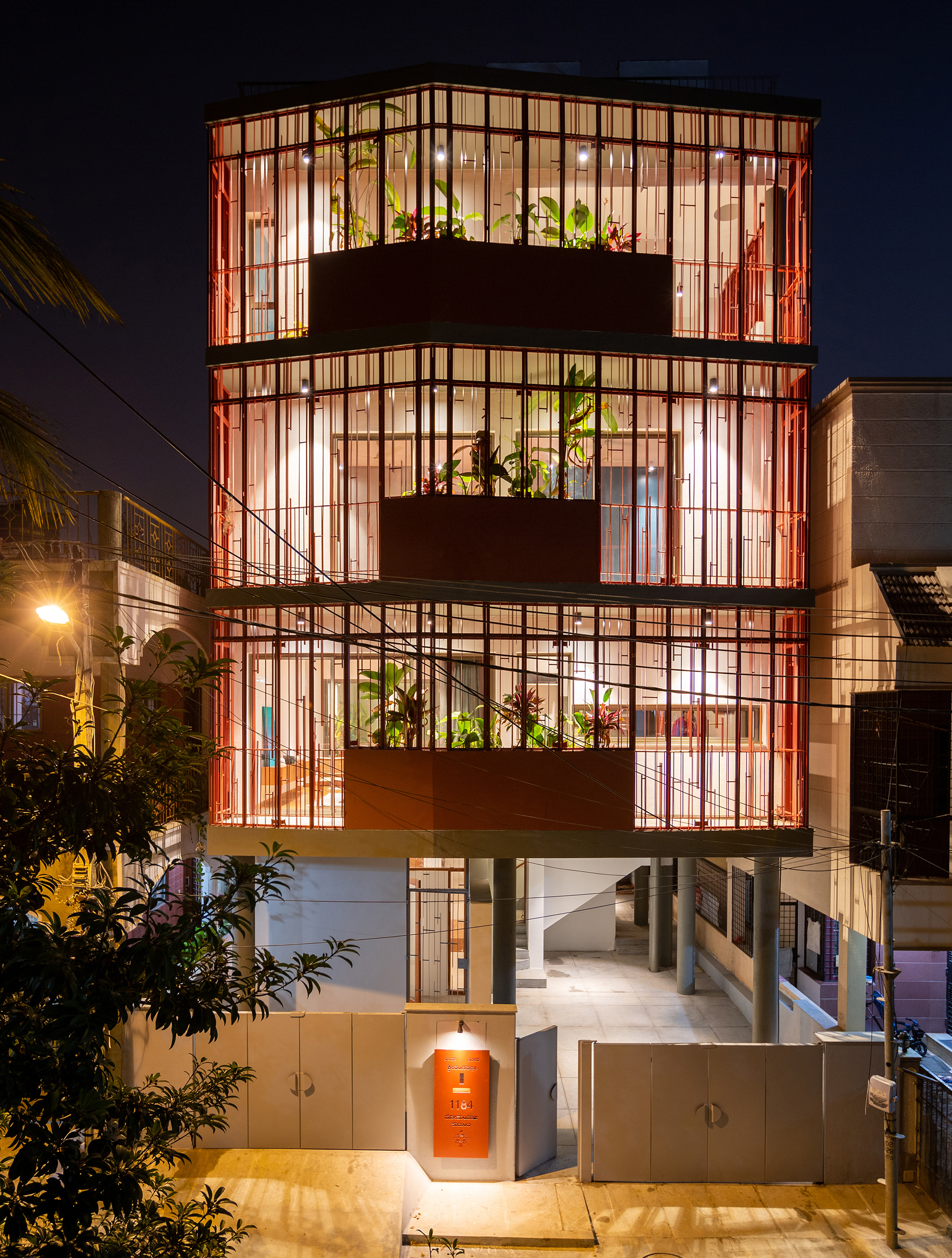 Night view of the stacked facade with illuminated vertical metal grid screens and planted balconies