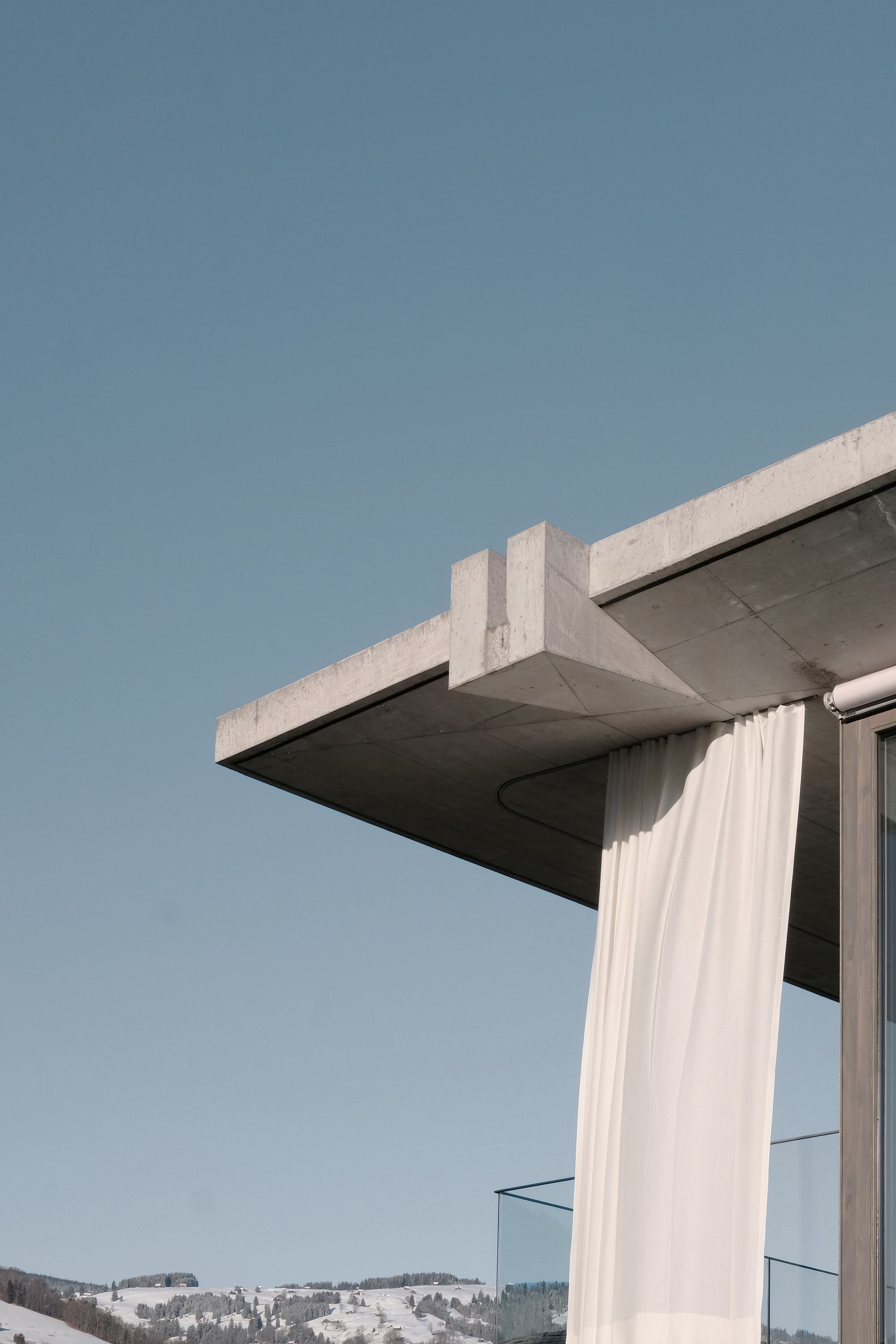 Close-up of the cantilevered concrete roof slab with white curtain billowing beside glazed corner