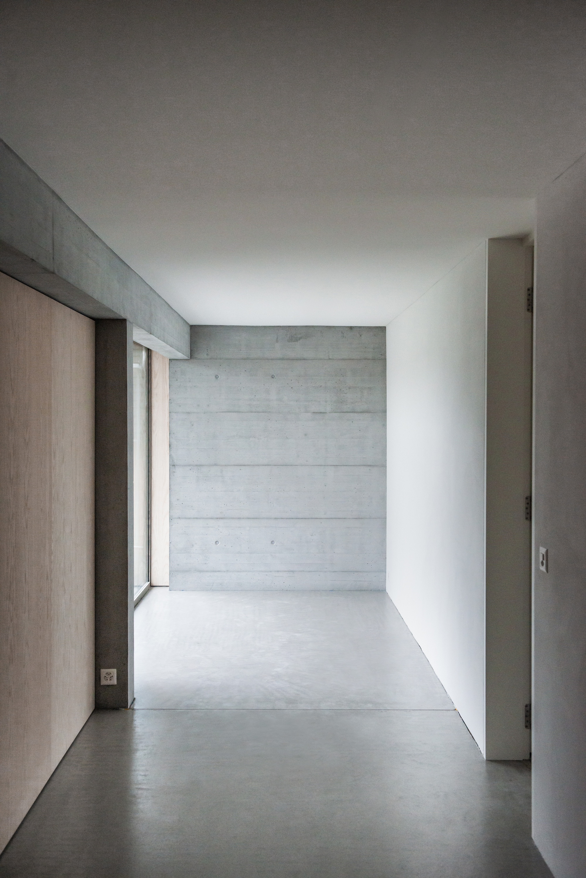 Interior corridor with board-formed concrete end wall and light oak wood panels along one side
